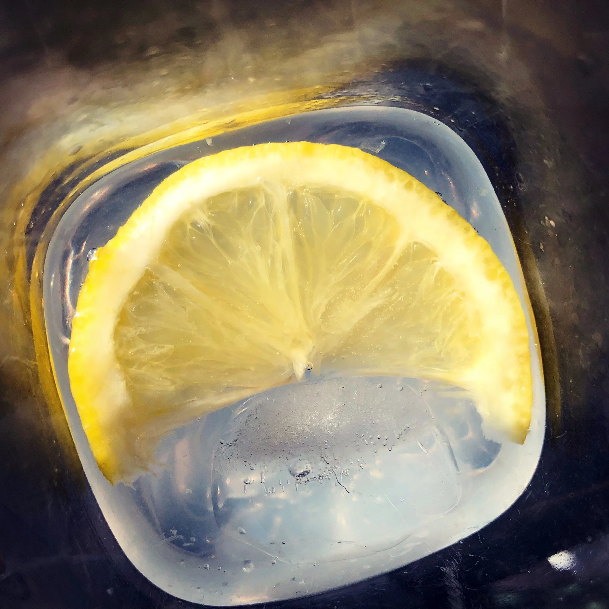 A slice of lemon floating in a clear liquid, inside a container or glass.