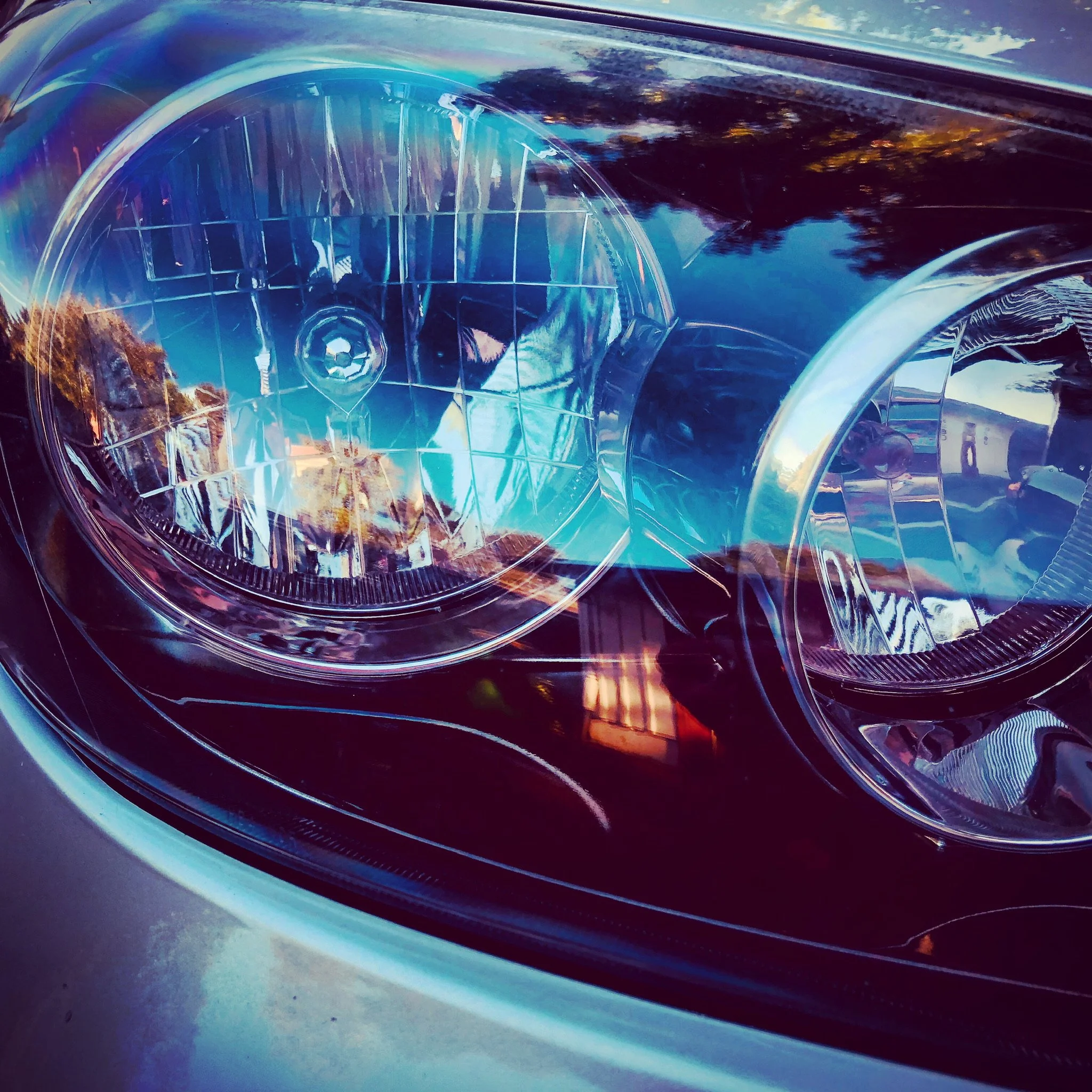 Close-up of a car's headlight reflecting trees and sky.
