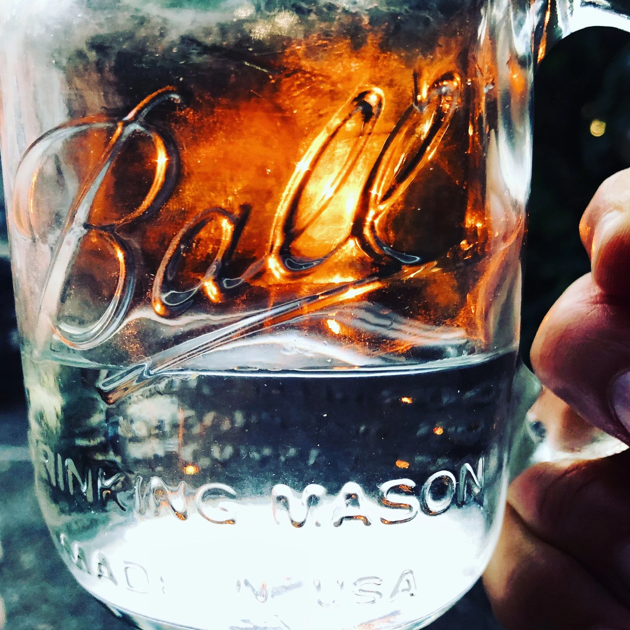 A clear glass mug with the words 'Jolson Whiskey' etched on it, filled with water and ice cubes, held by a person's hand.
