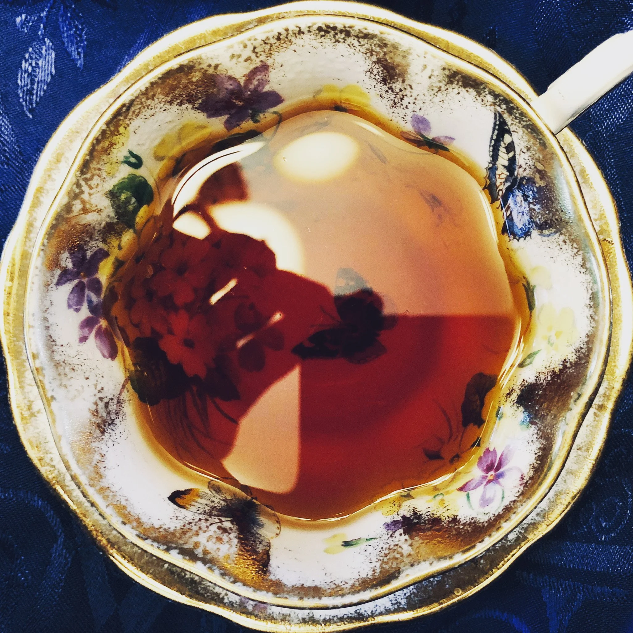 A floral porcelain teacup filled with dark tea, placed on a matching saucer on a dark blue, textured cloth.