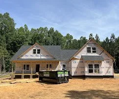 Construction site with a house under building, surrounded by trees and a blue sky.