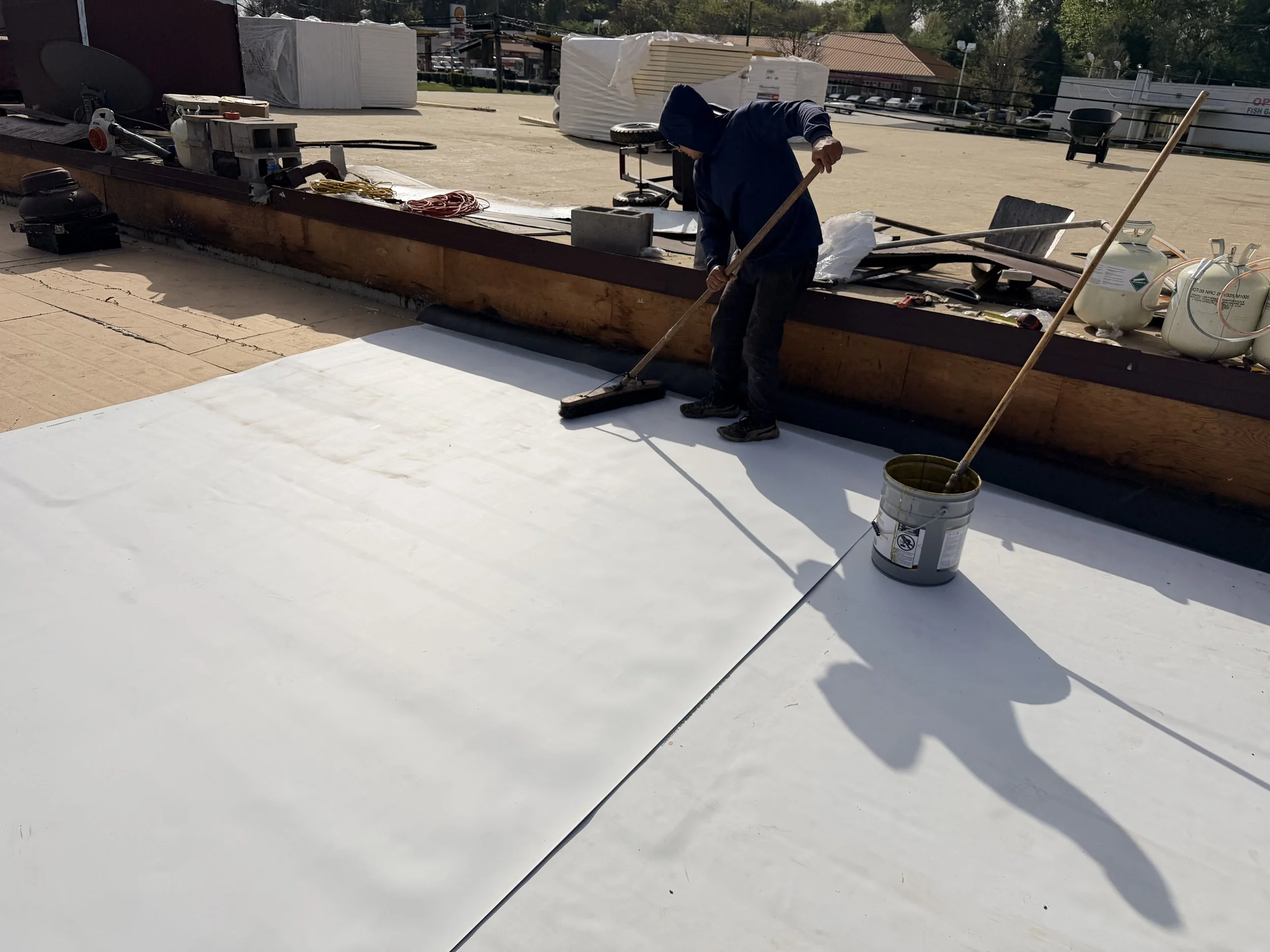A person in a hoodie sweeping the rooftop of a building with construction materials, tools, and equipment around.