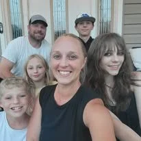 A group of five people, including adults and children, smiling together outside a house.