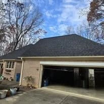 Front of a two-car garage attached to a house, with the garage door open, brick exterior, and a paved driveway, under a clear blue sky.