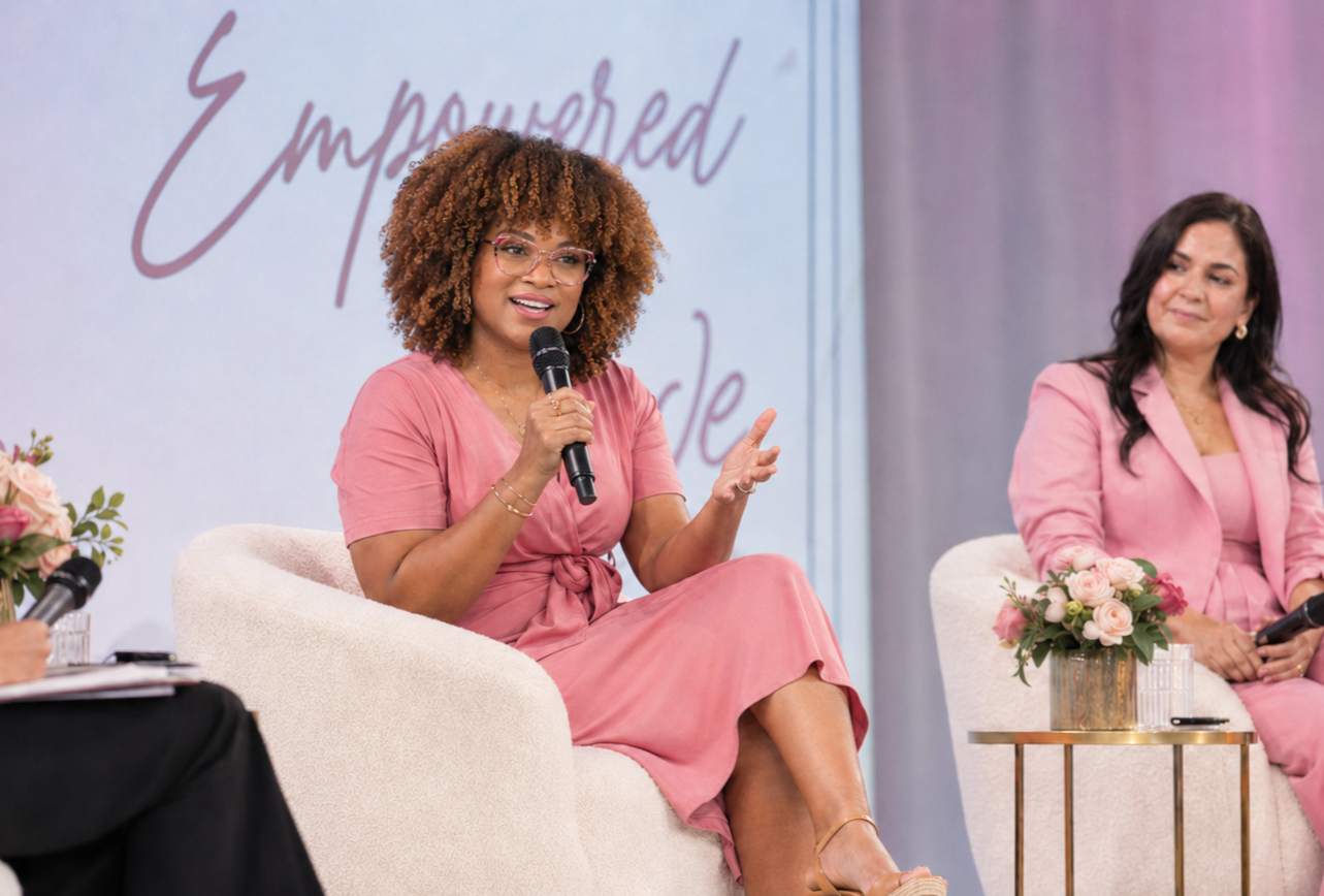 Keisha Gaddis sitting on a stage with a light pink dress speaking into a microphone.