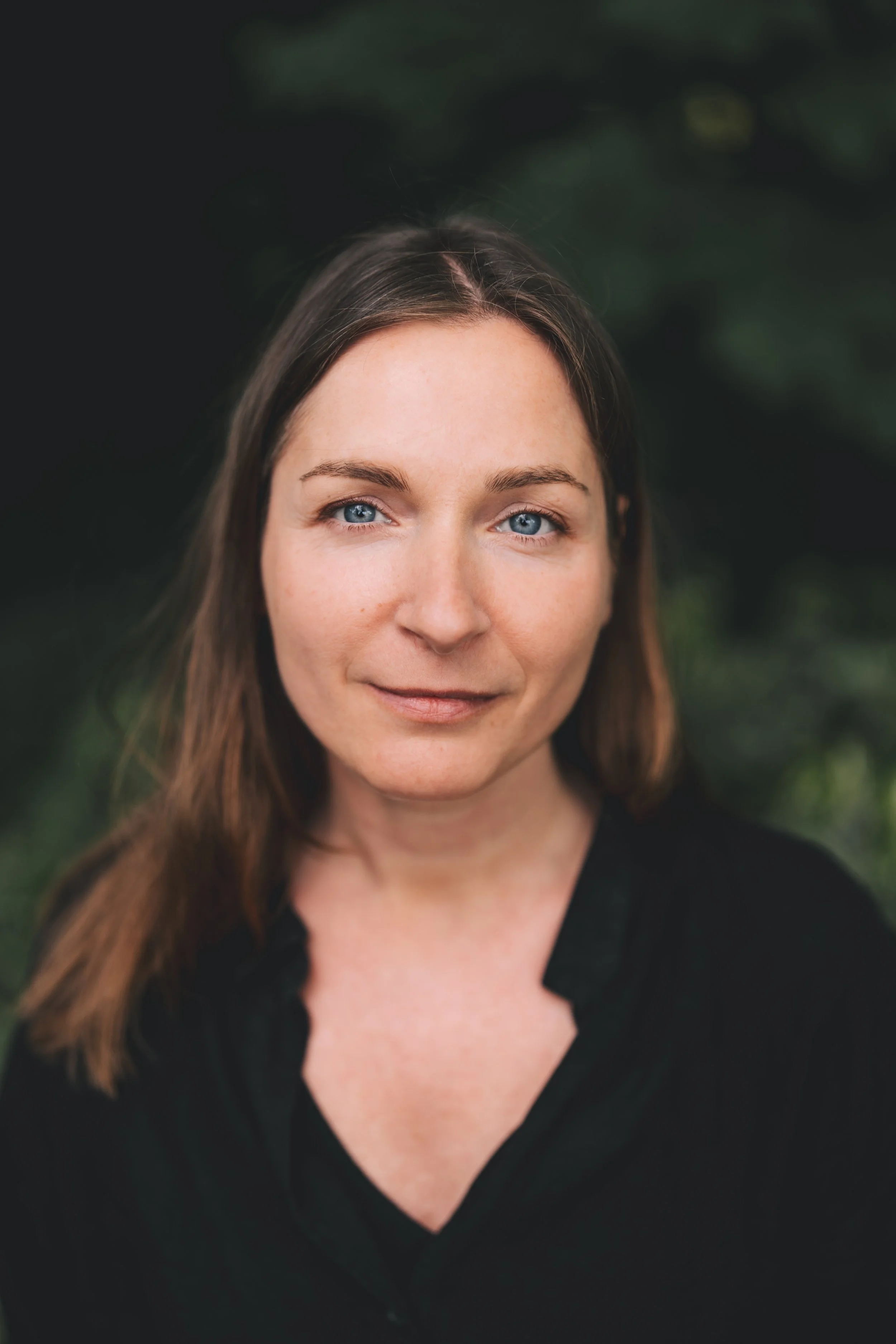 Nahaufnahme einer jungen Frau mit braunen Haaren und blauen Augen vor einem grünen, unscharfen Hintergrund.