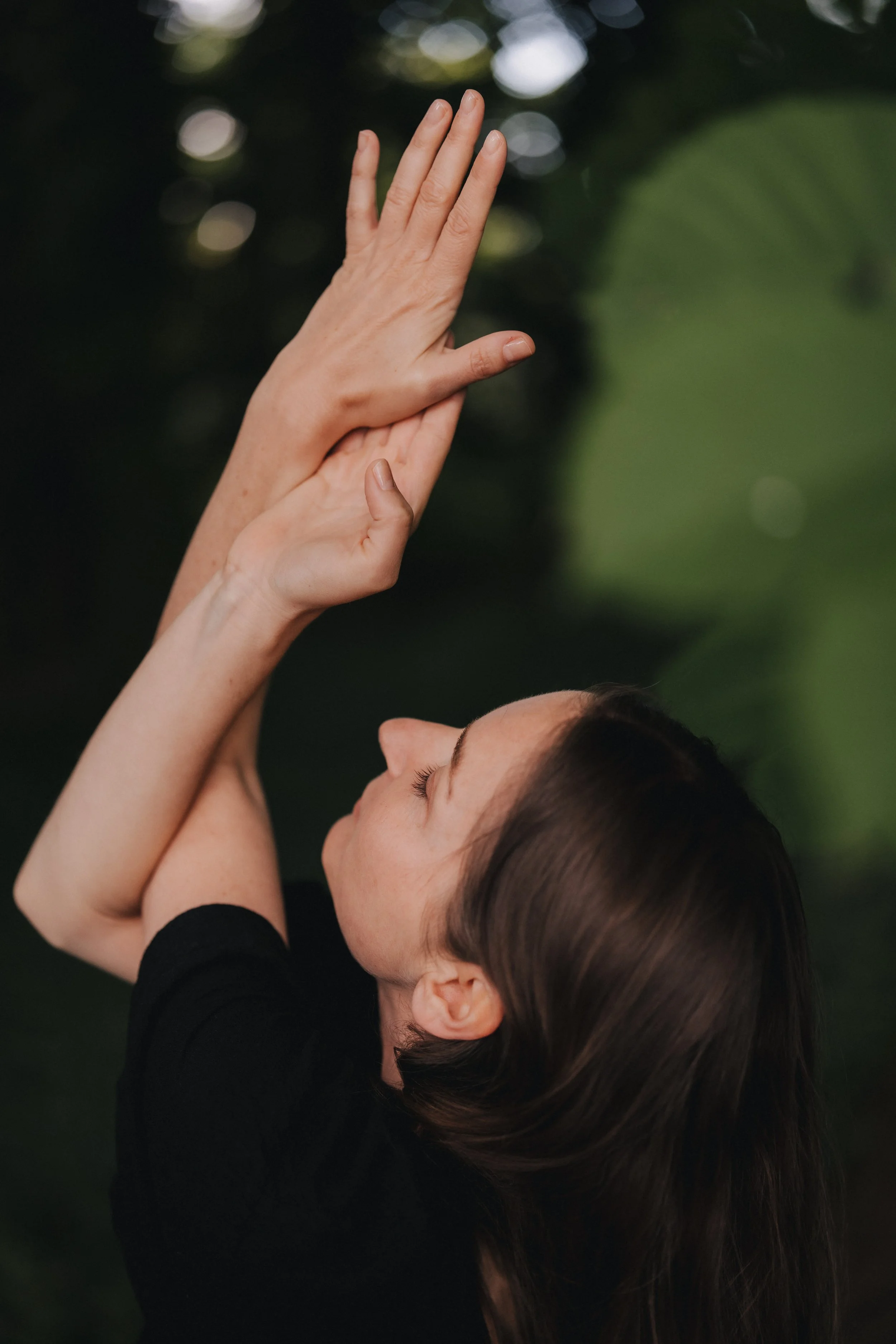 Eine Frau mit dunklen Haaren führt einen Yoga-Posen im Freien aus, mit den Händen vor dem Gesicht und den Augen geschlossen.