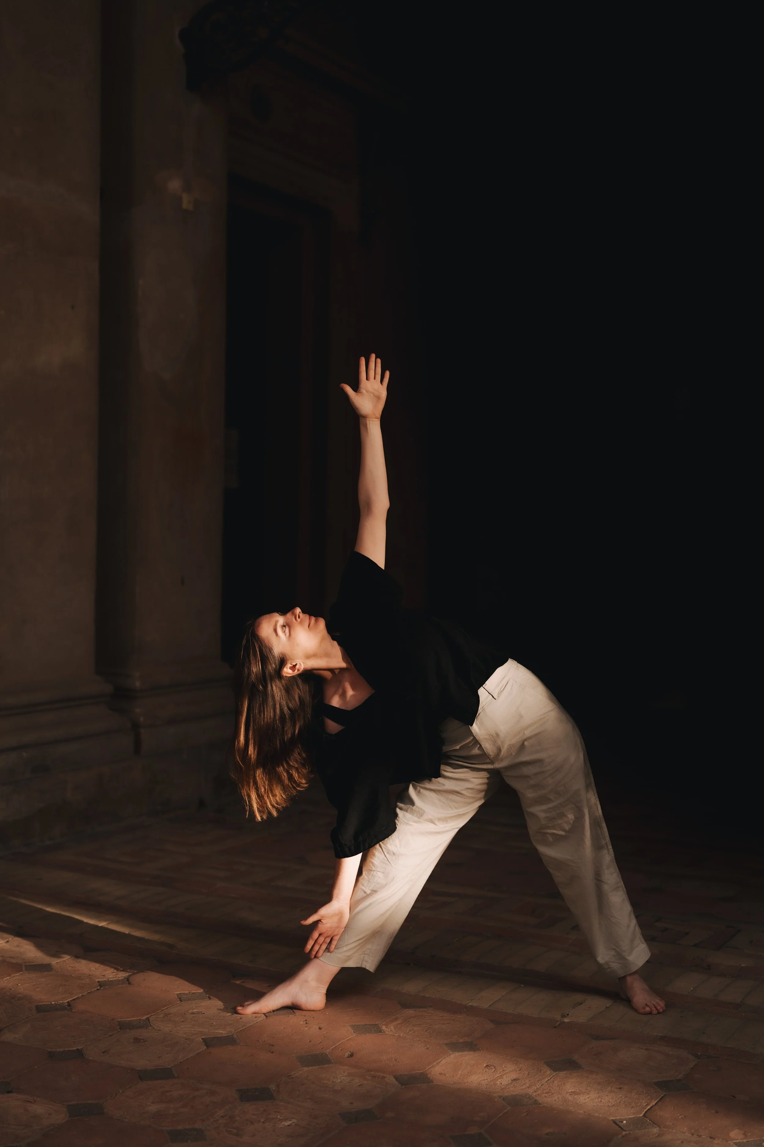Frau in Schwarz und Weiß, die eine Tanzpose in einem dunklen Raum macht, mit Blick nach oben und einem Arm in die Luft gestreckt.