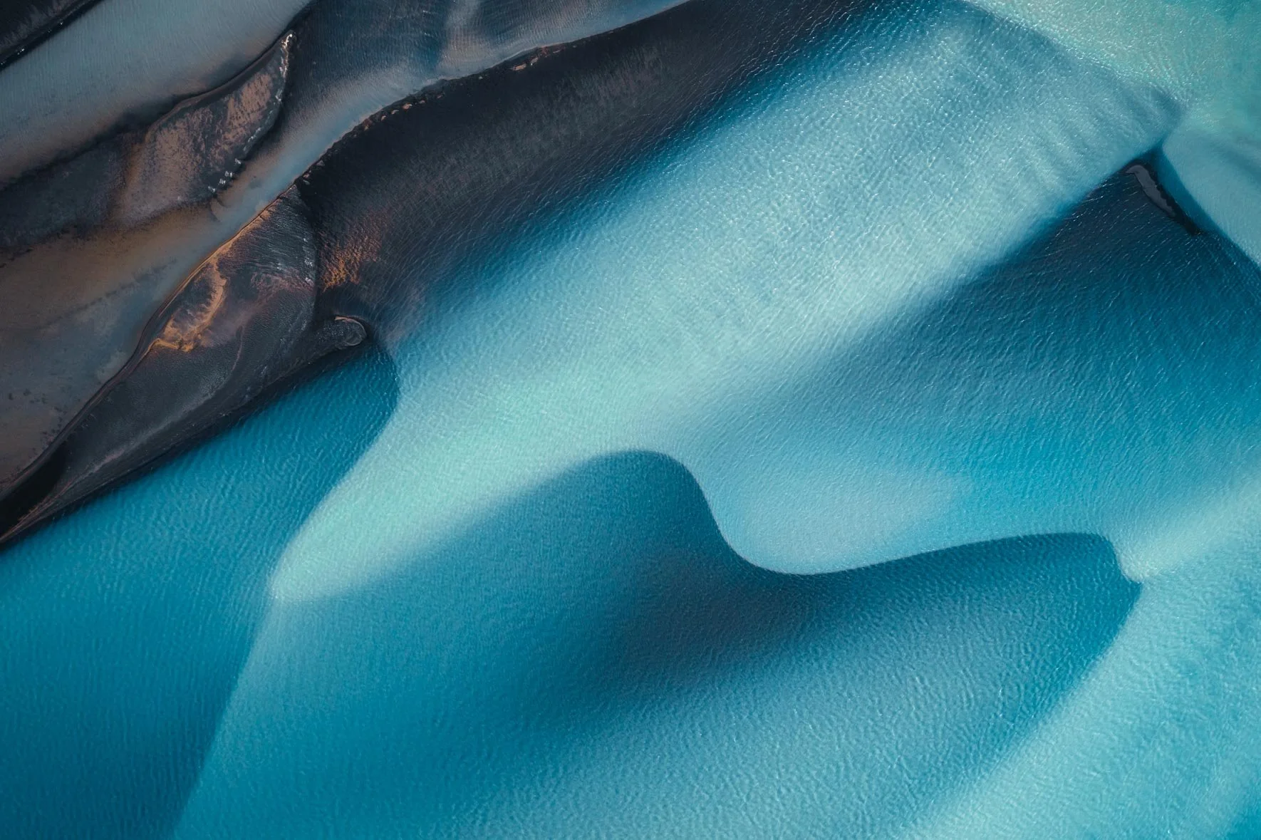 Close-up view of a river in Iceland with creases and folds, featuring dark, shiny areas and light reflections.