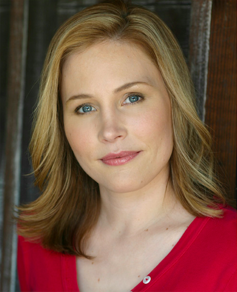 Close-up portrait of a woman with blonde hair and blue eyes, wearing a red top, in front of a wooden background.