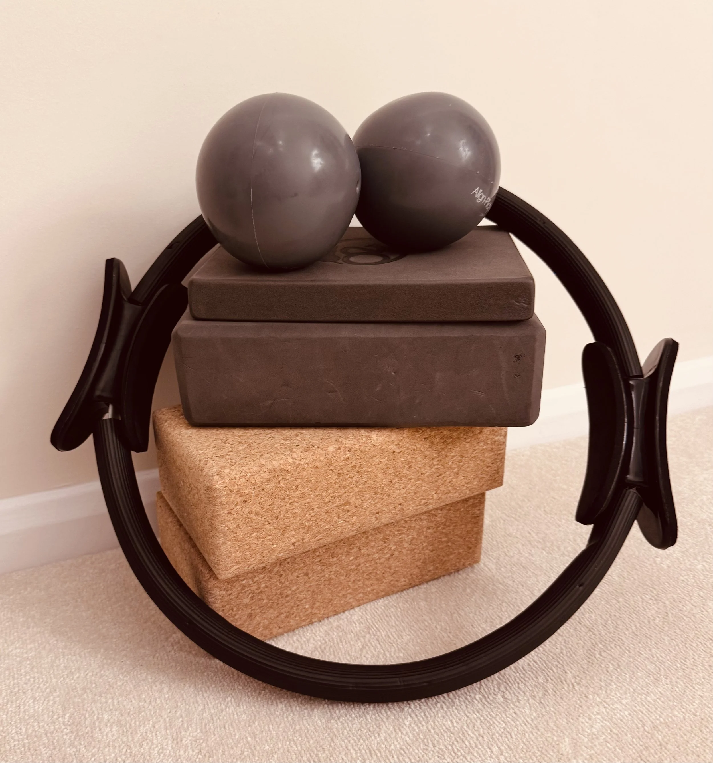 Exercise equipment including a yoga wheel, two yoga blocks, and two massage balls stacked on a carpeted floor.