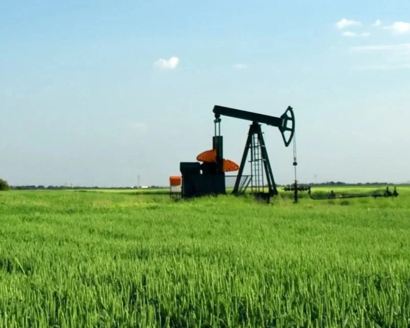 Oil pump jack in a green field with a clear blue sky