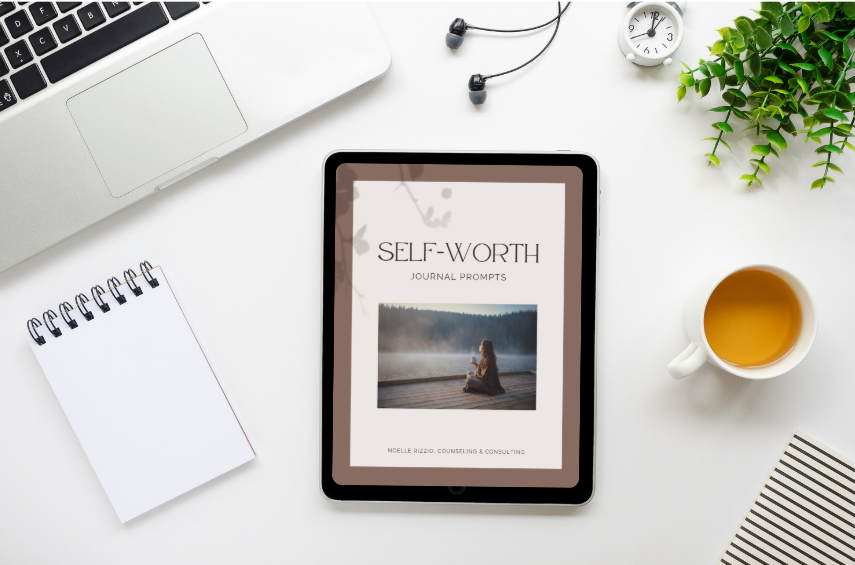 A flat lay of a workspace with a laptop, a notepad, wired earphones, a clock, a plant, a cup of tea, and a tablet displaying a journal prompt titled 'Self-Worth for Moms'.