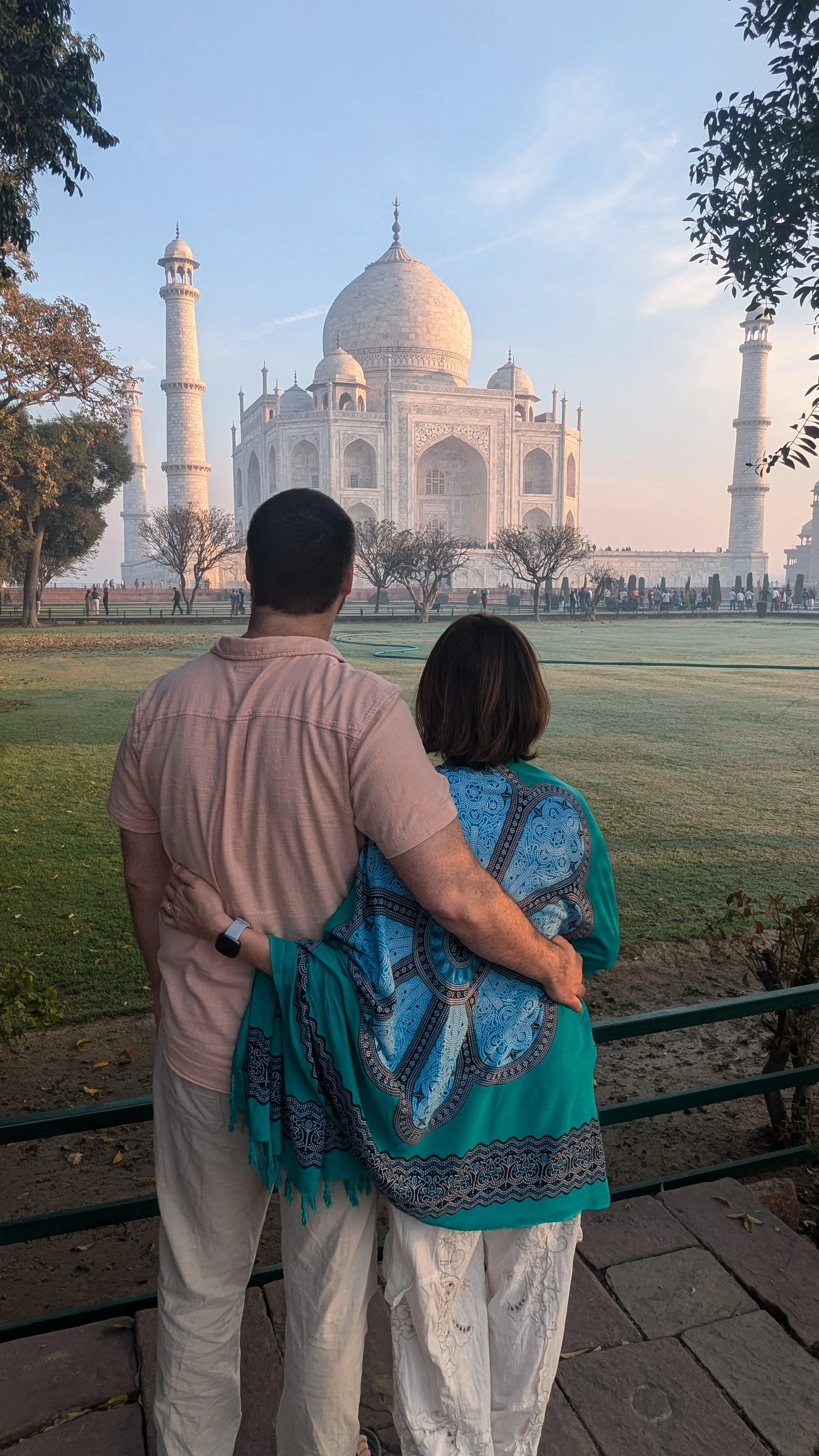 A couple standing in front of the Taj Mahal, an iconic white marble mausoleum in India, during sunset.