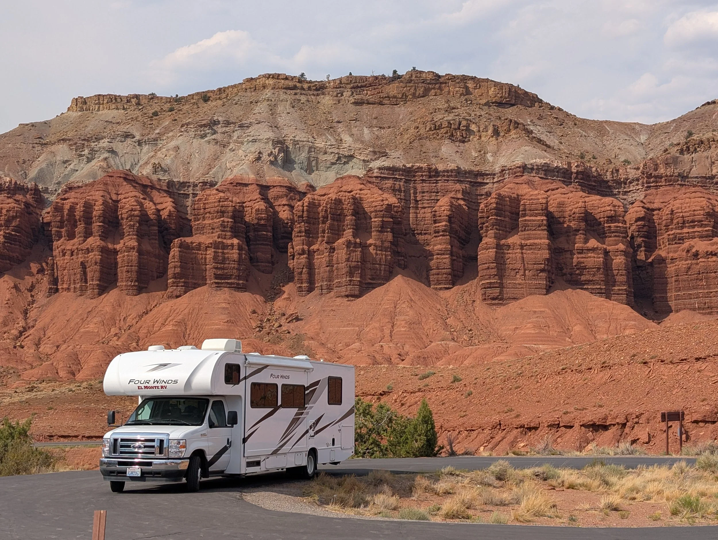 A white recreational vehicle parked on a curved road with colorful red and brown canyon cliffs in the background.