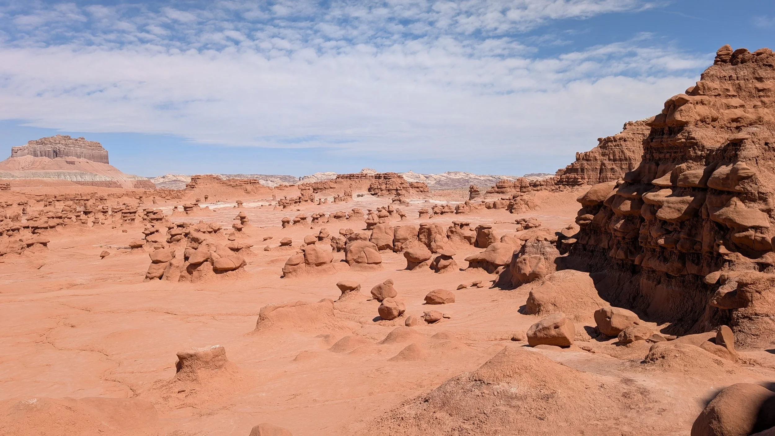 A desert landscape with numerous small and large rock formations under a partly cloudy blue sky.