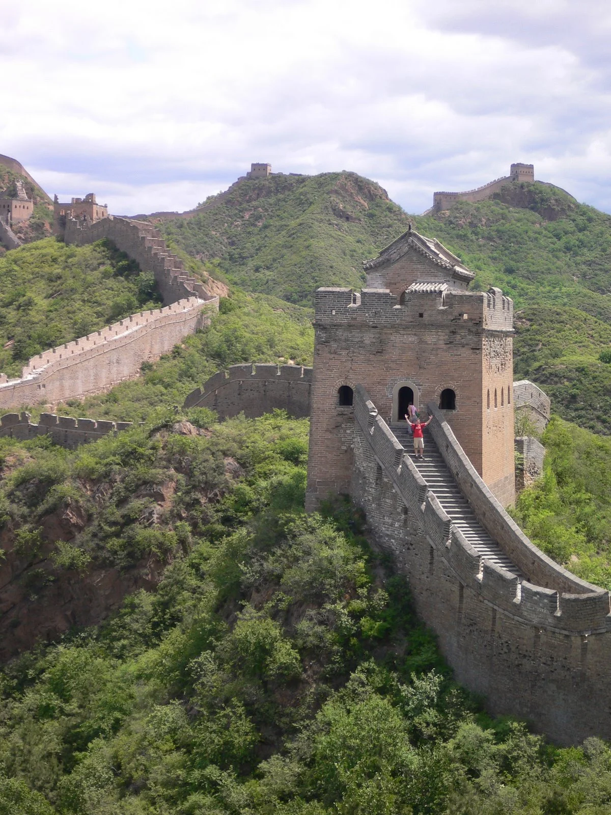 The Great Wall of China extending across green mountains with a watchtower and visitors taking photos.