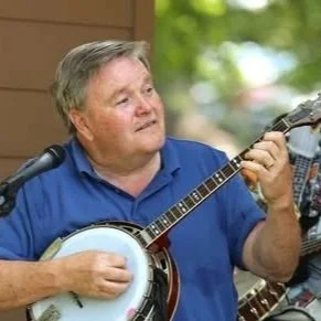 A man playing a banjo and singing into a microphone outdoors.