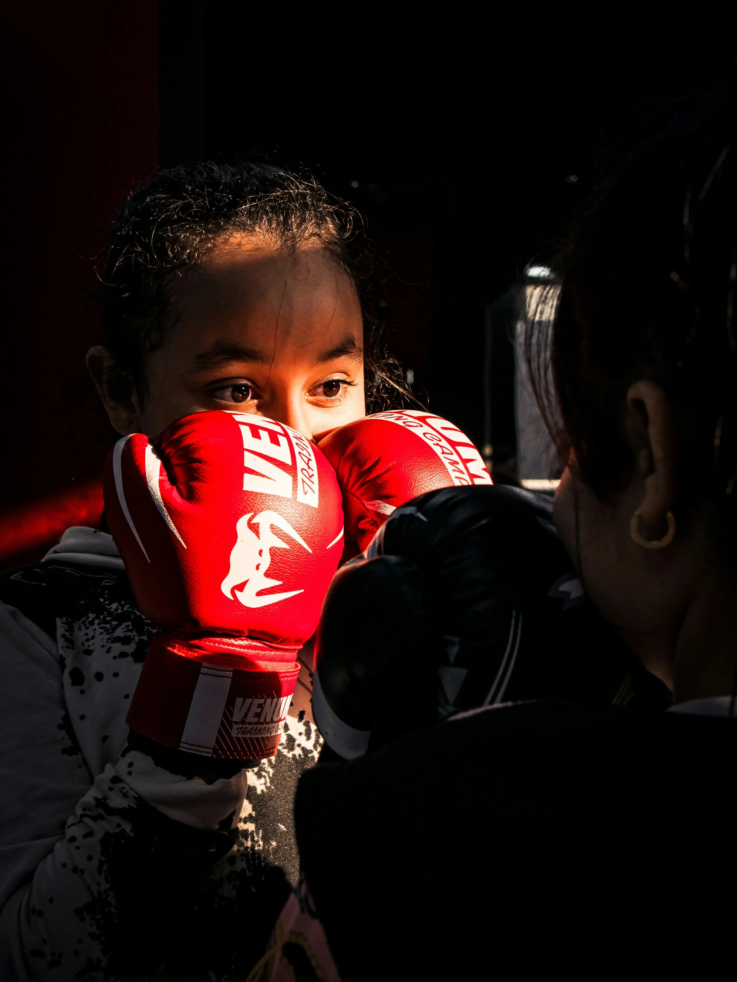 Young girl wearing red boxing gloves training with an older woman in a boxing stance.