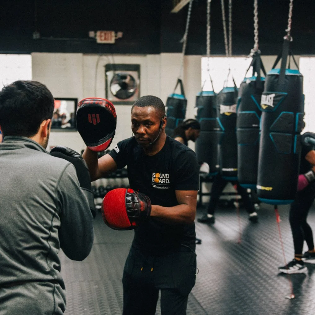 Man practicing boxing with trainer in a gym, surrounded by punching bags.