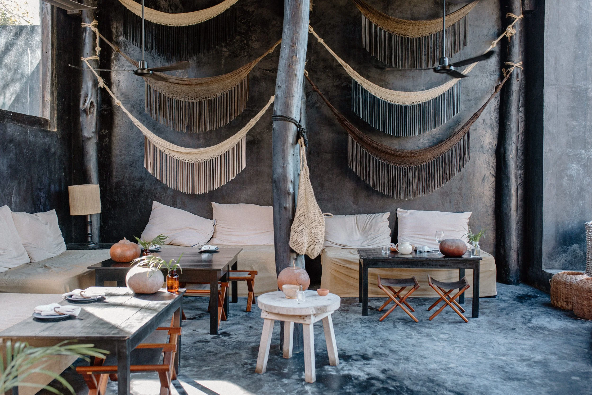 Interior of a modern, rustic living space or lounge with hanging fabric or net decorations on a dark, textured wall, and various furniture pieces including sofas, tables, and rugs.