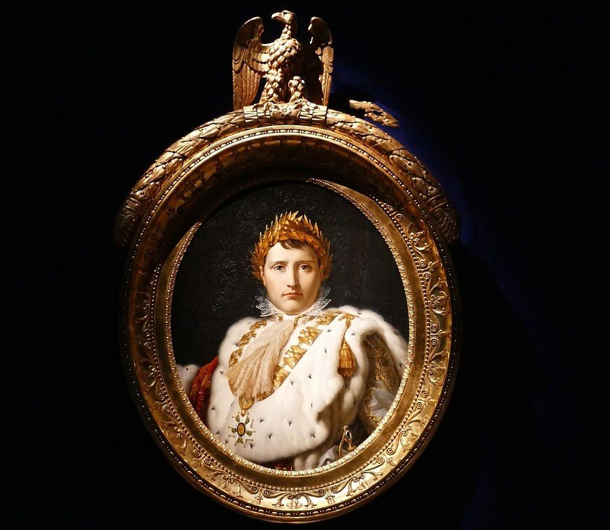 Portrait of a young person with a crown, dressed in royal attire with a fur cloak, displayed in an ornate gold frame with an eagle at the top.