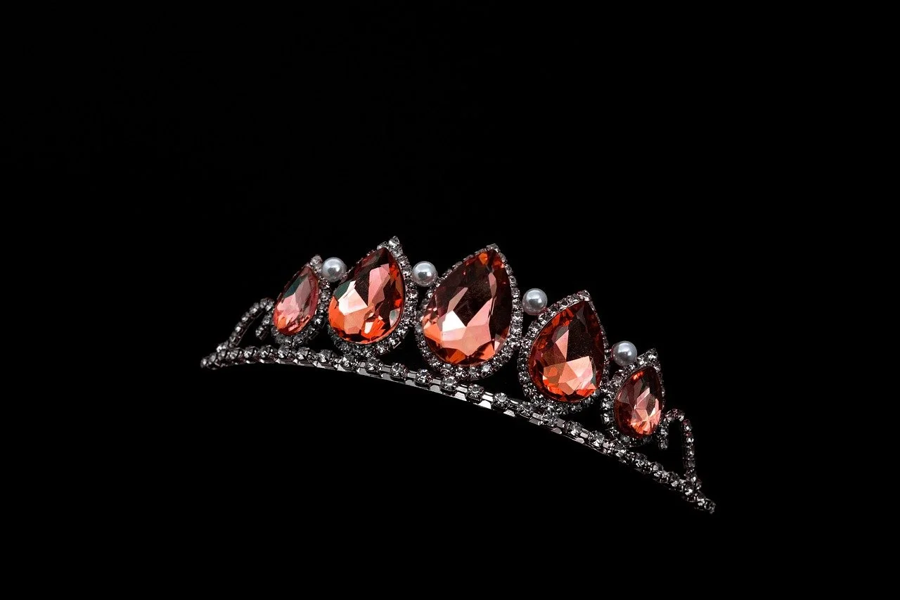 A tiara with large peach-colored gemstones, small white pearls, and clear rhinestones on a black background.