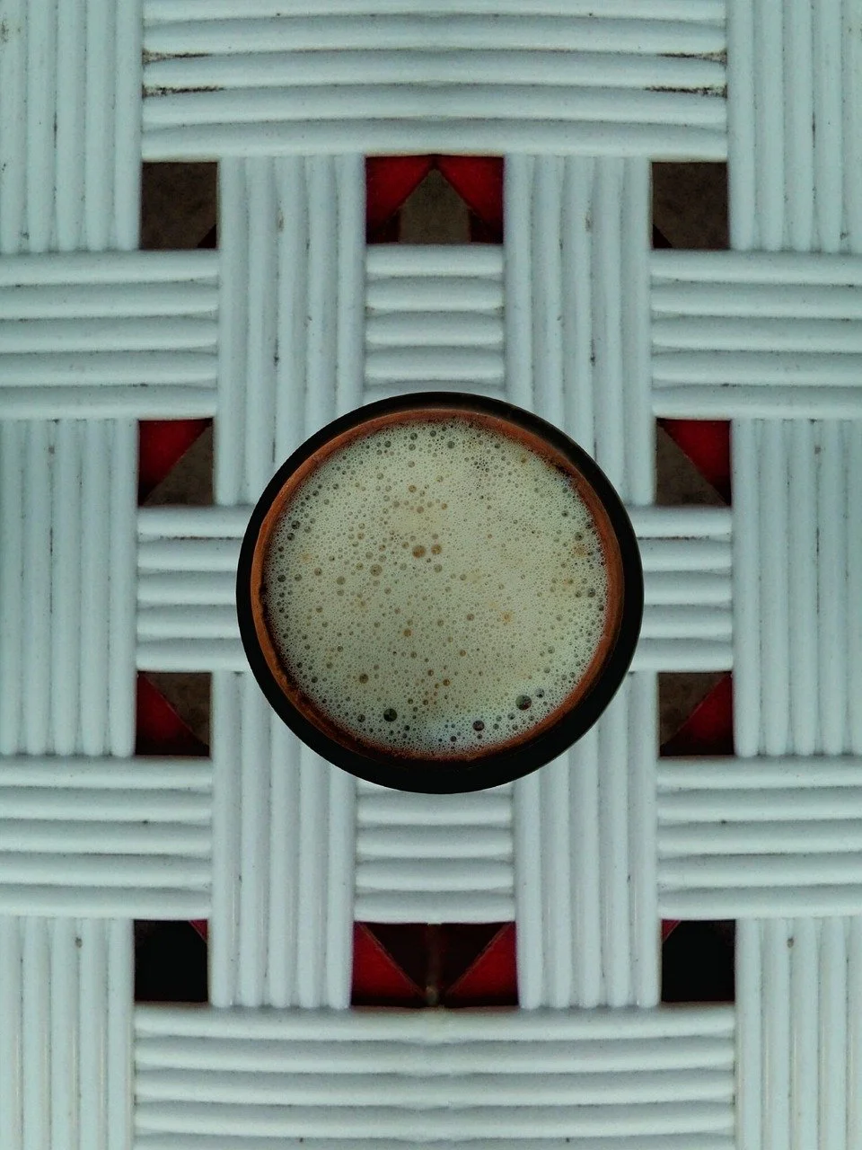 A bowl of frothy green tea placed on a woven white and red surface seen from above.