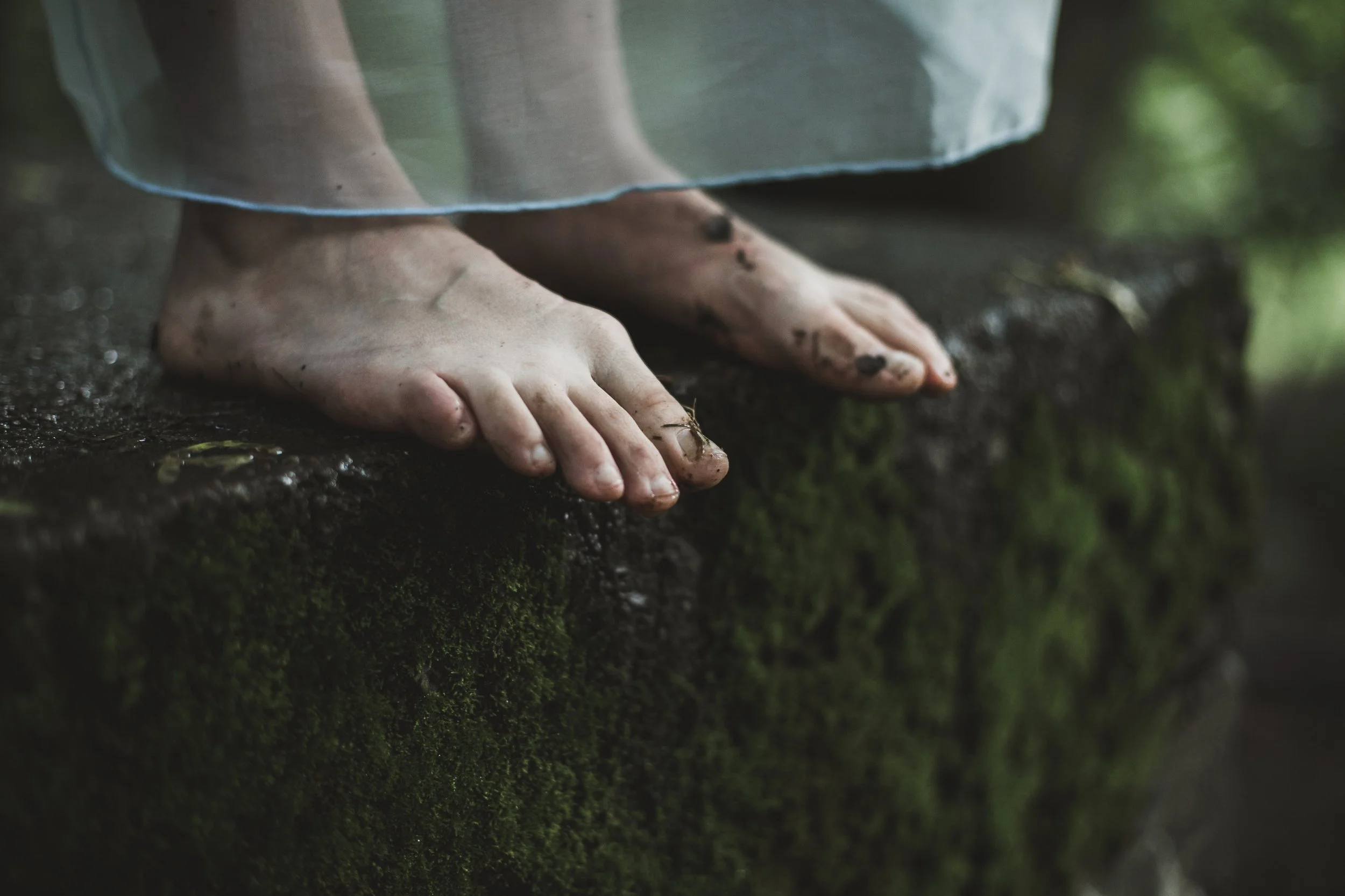 Close-up of bare feet standing on a moss-covered ground and the bottom of a shear flowy skirt.