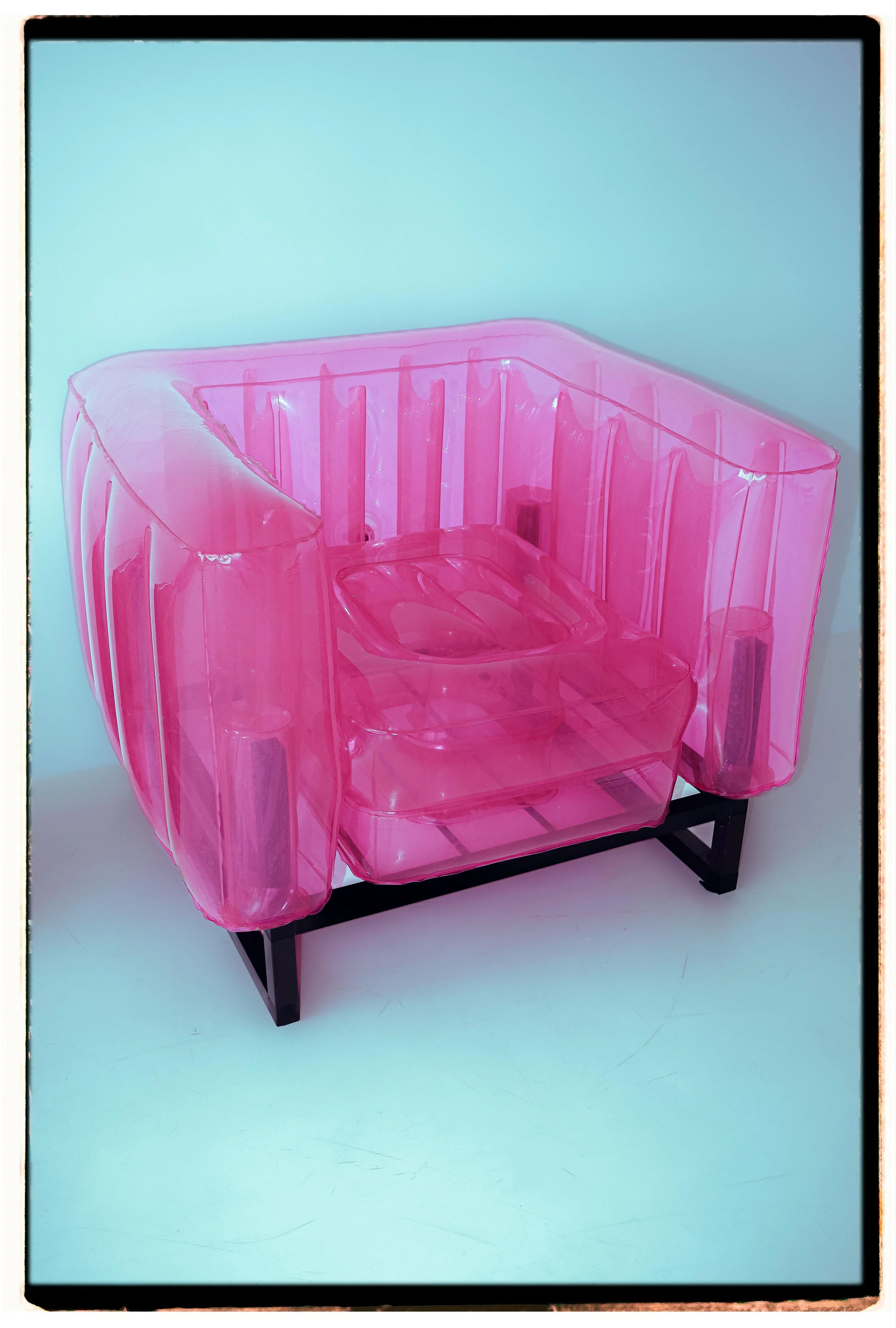 A pink transparent plastic chair with armrests, set on a black metal frame, against a plain white background.