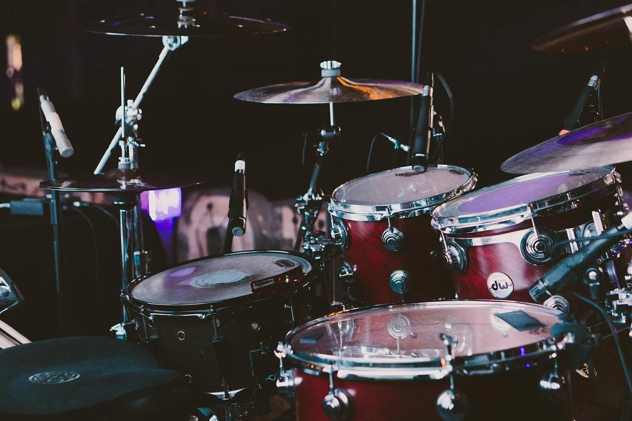 A red drum set with black drumheads on a music stage, with cymbals and microphones.