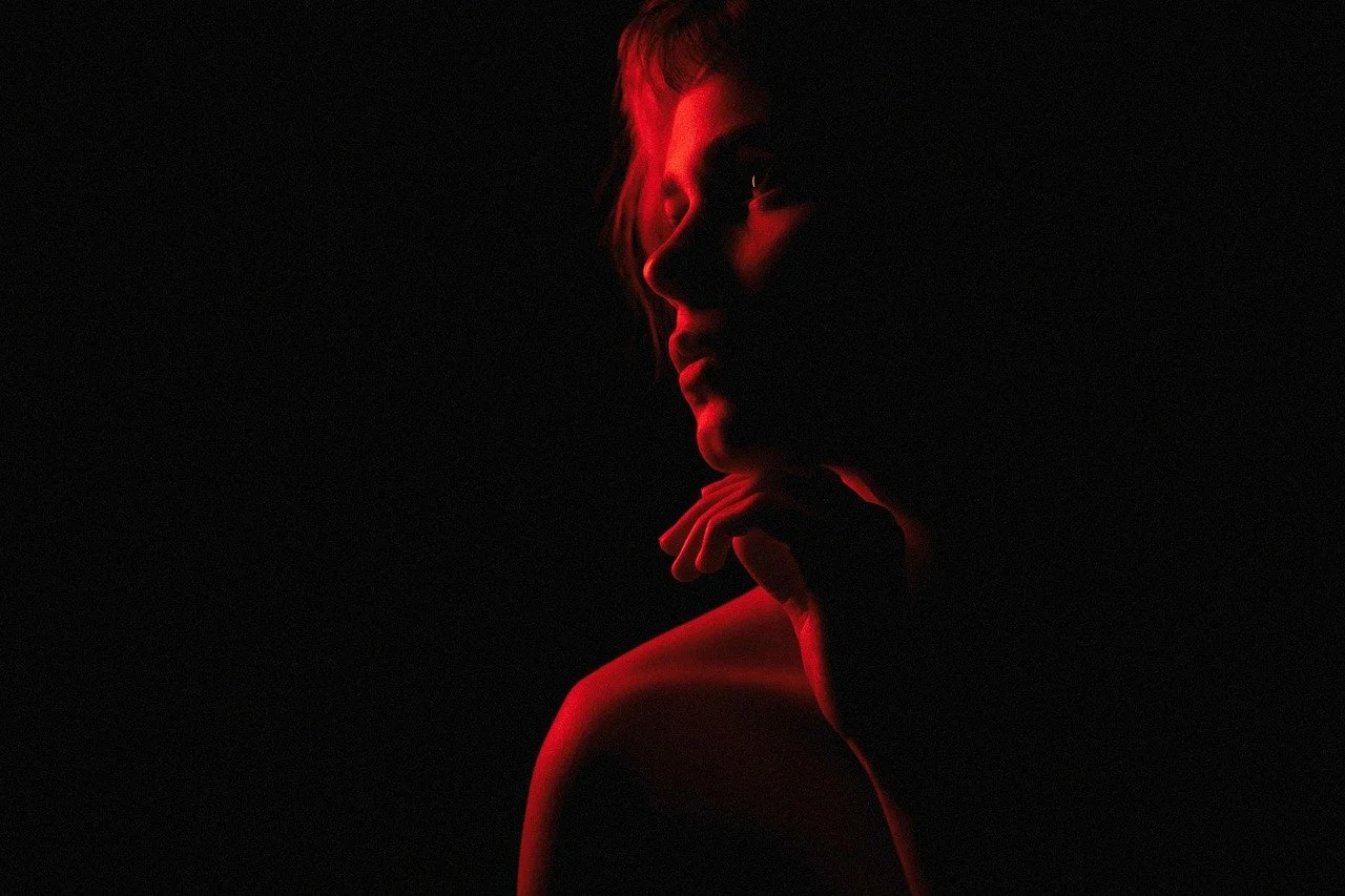A woman with short hair is illuminated by red light, creating a silhouette against a dark background.