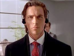 A still from the 2000 film, American Psycho, with main character Patrick Bateman in a suit with a red tie and over the ear headphones