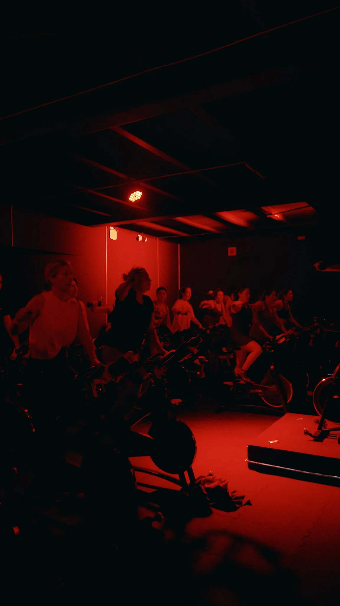 Grupo de personas en una clase de spinning en una sala con iluminación roja.