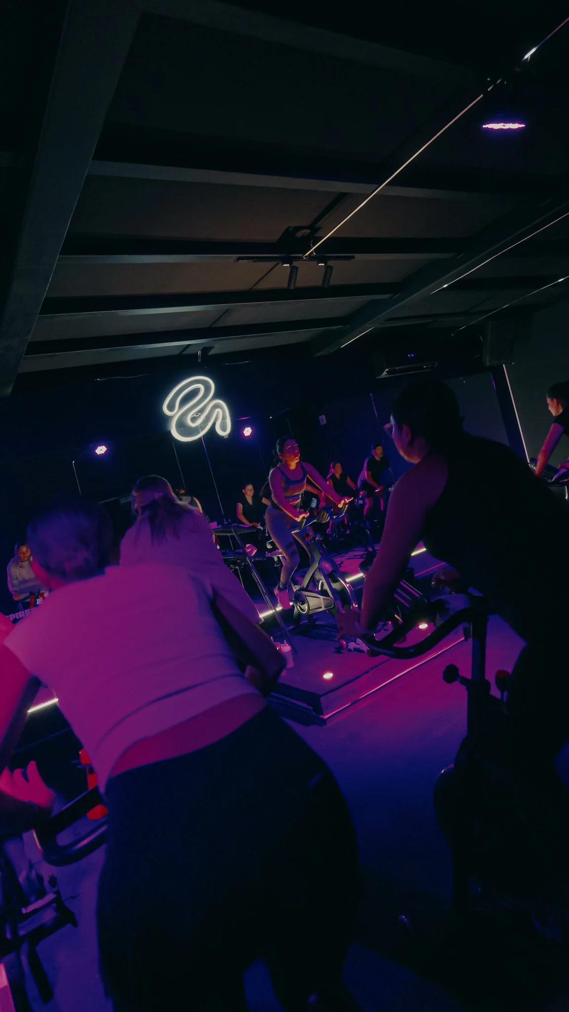 Grupo de personas participando en una clase de spinning en un gimnasio con iluminación de colores
