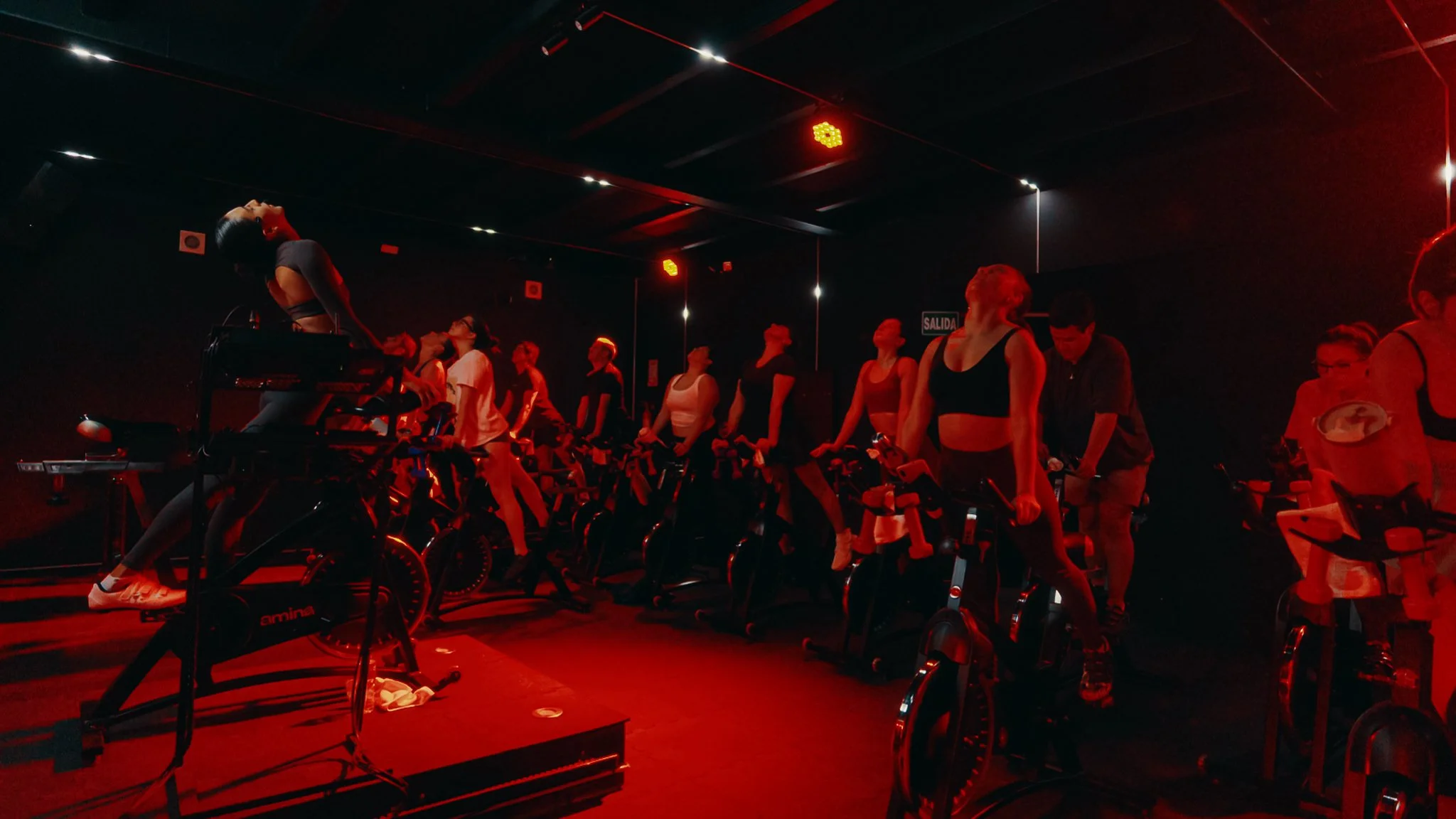 Clase de cycling con varias personas pedaleando en bicicletas estacionarias en una sala con iluminación roja.