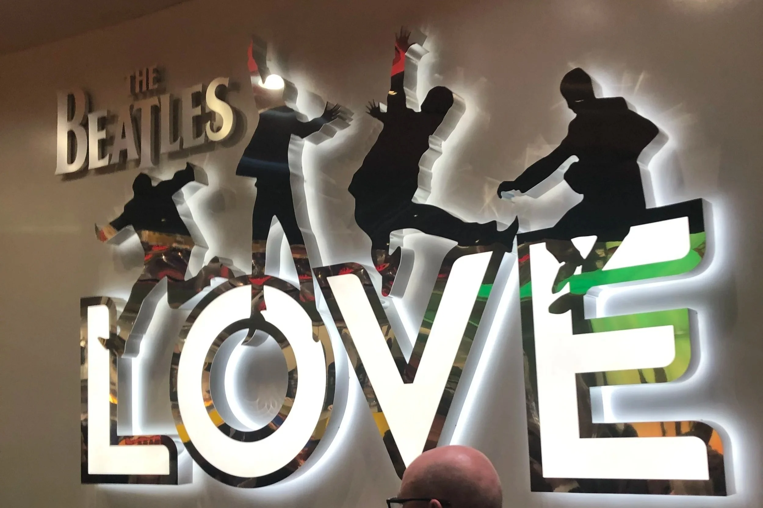 Silhouette cutouts of The Beatles members performing, with the word 'LOVE' in large letters, illuminated by backlighting.