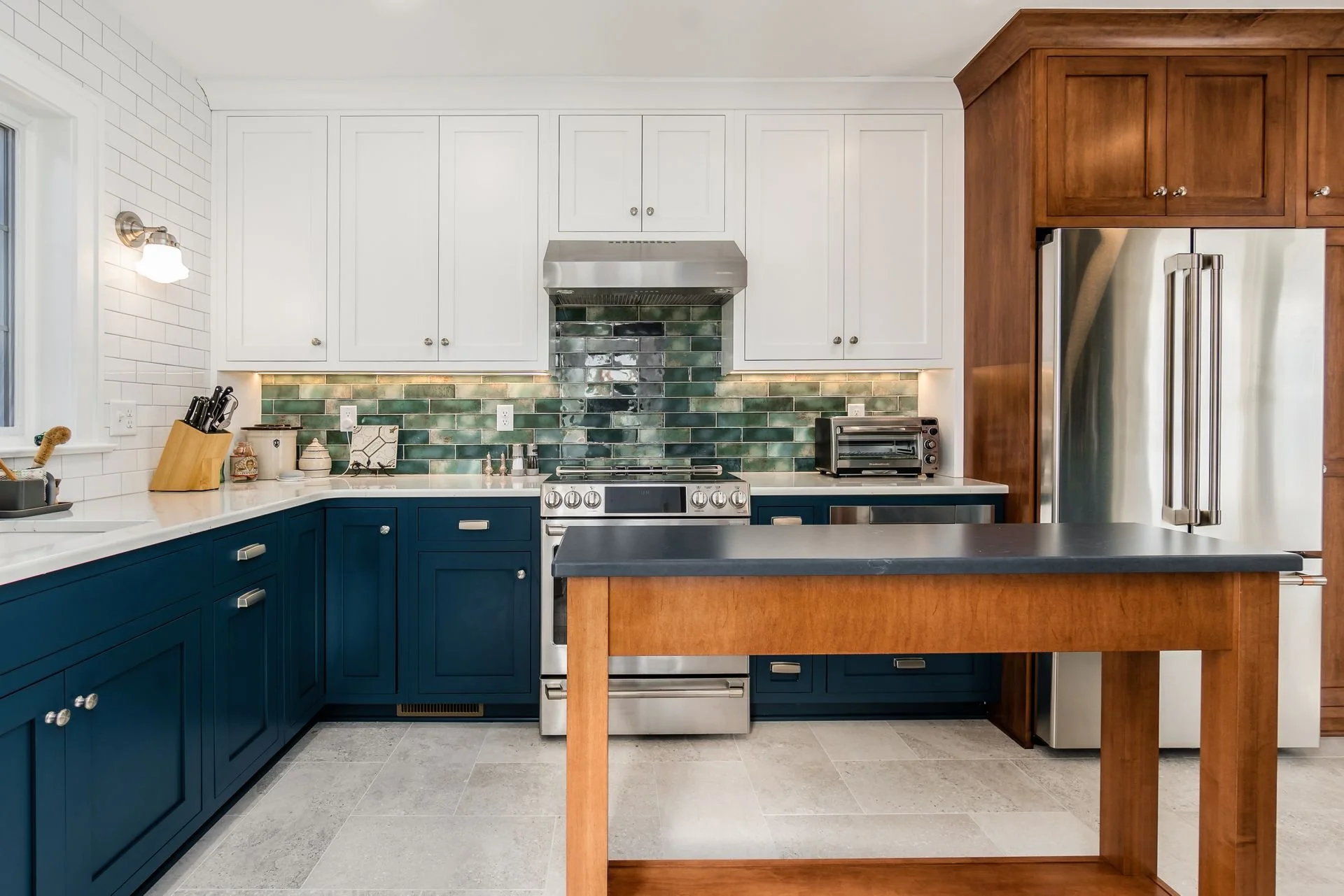 Central Ohio kitchen remodel featuring navy lower cabinets, white uppers, warm wood pantry cabinetry, and handcrafted green tile backsplash by Residence.