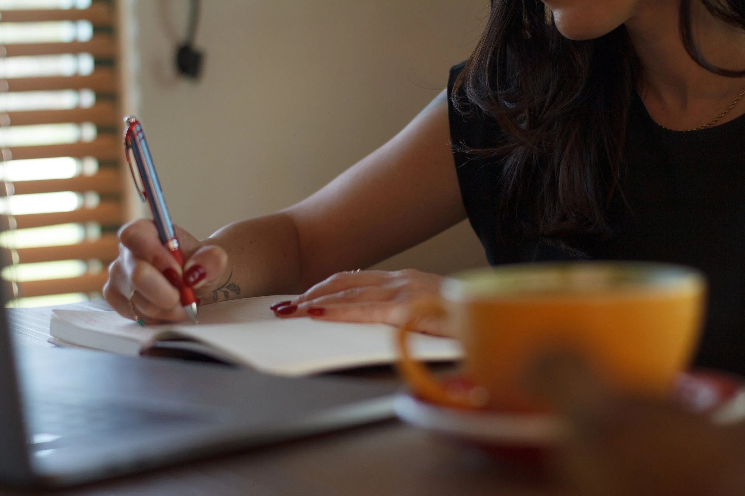 Desiree Polonis, LCSW journaling at a table with tea, symbolizing mindfulness, reflection and grounded therapeutic support.