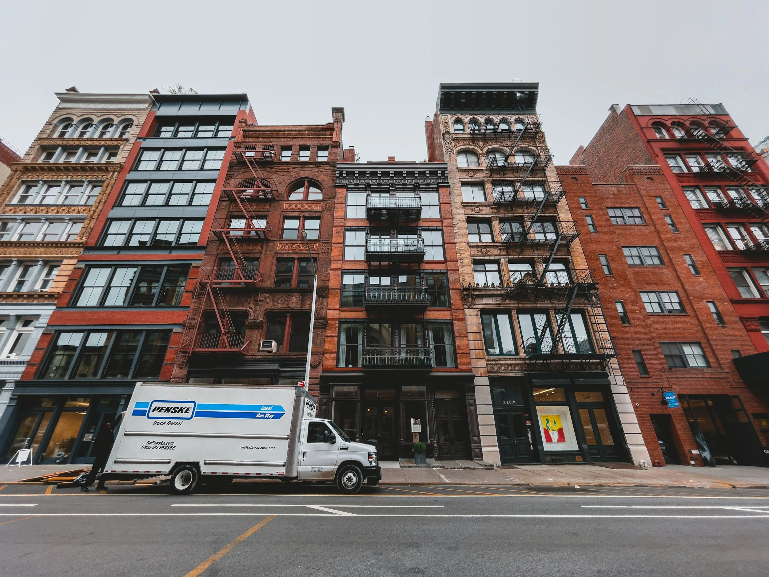 City street with tall brick and glass buildings and a white delivery truck parked on the side.
