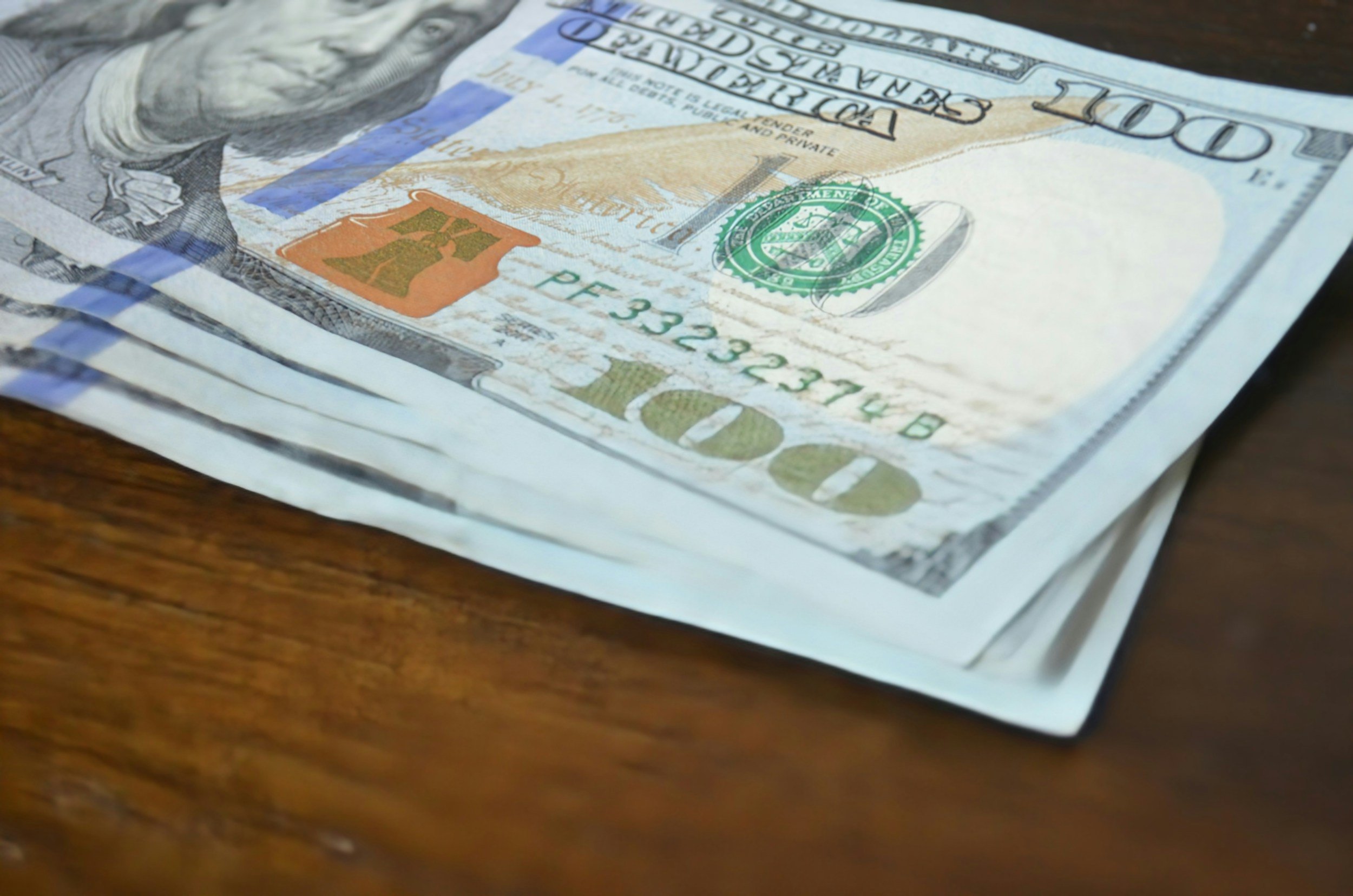 Close-up of a stack of U.S. hundred-dollar bills on a wooden surface.