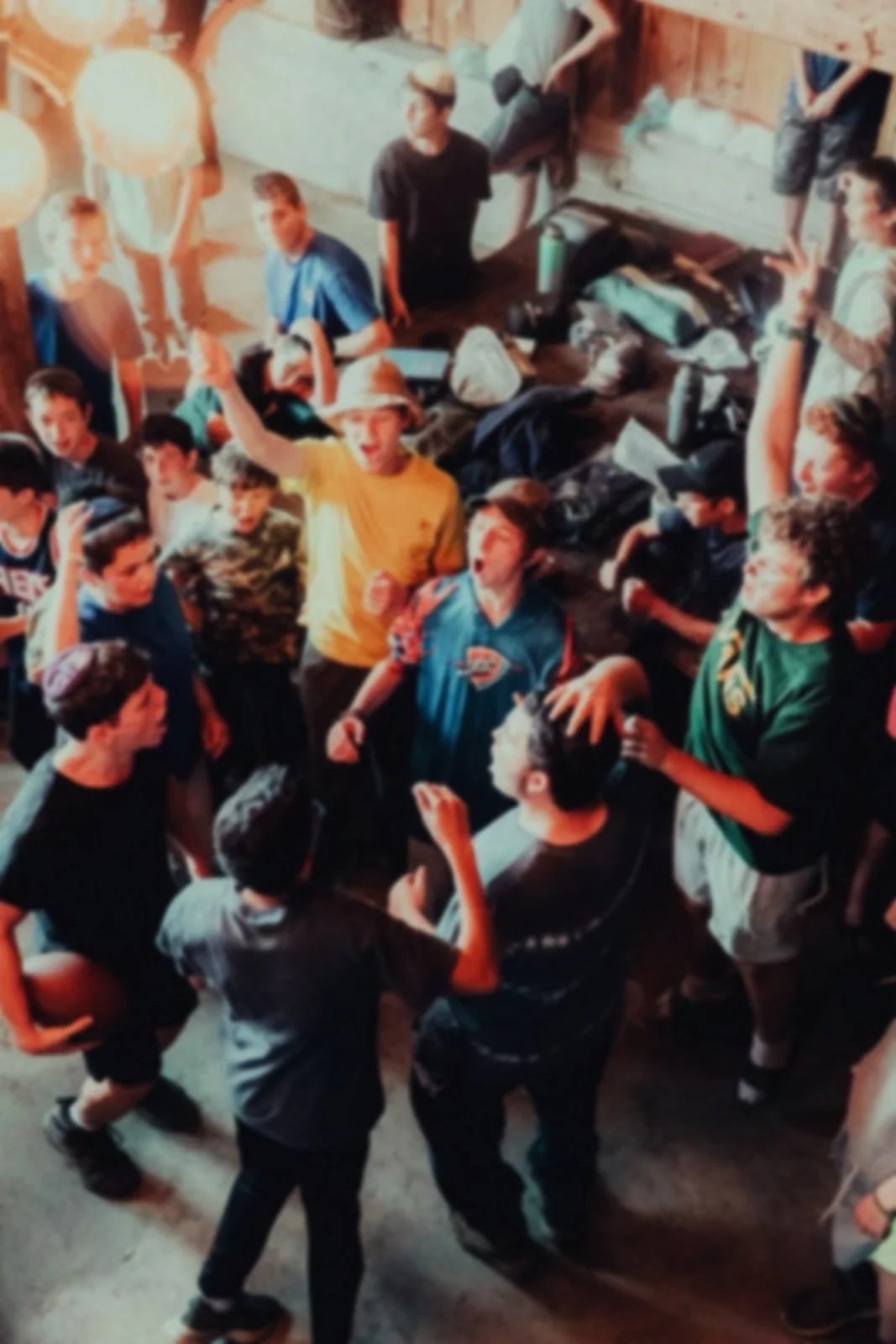 A group of boys gathered inside a wooden cabin or lodge, some standing and some sitting on the floor, engaging in conversation and socializing.