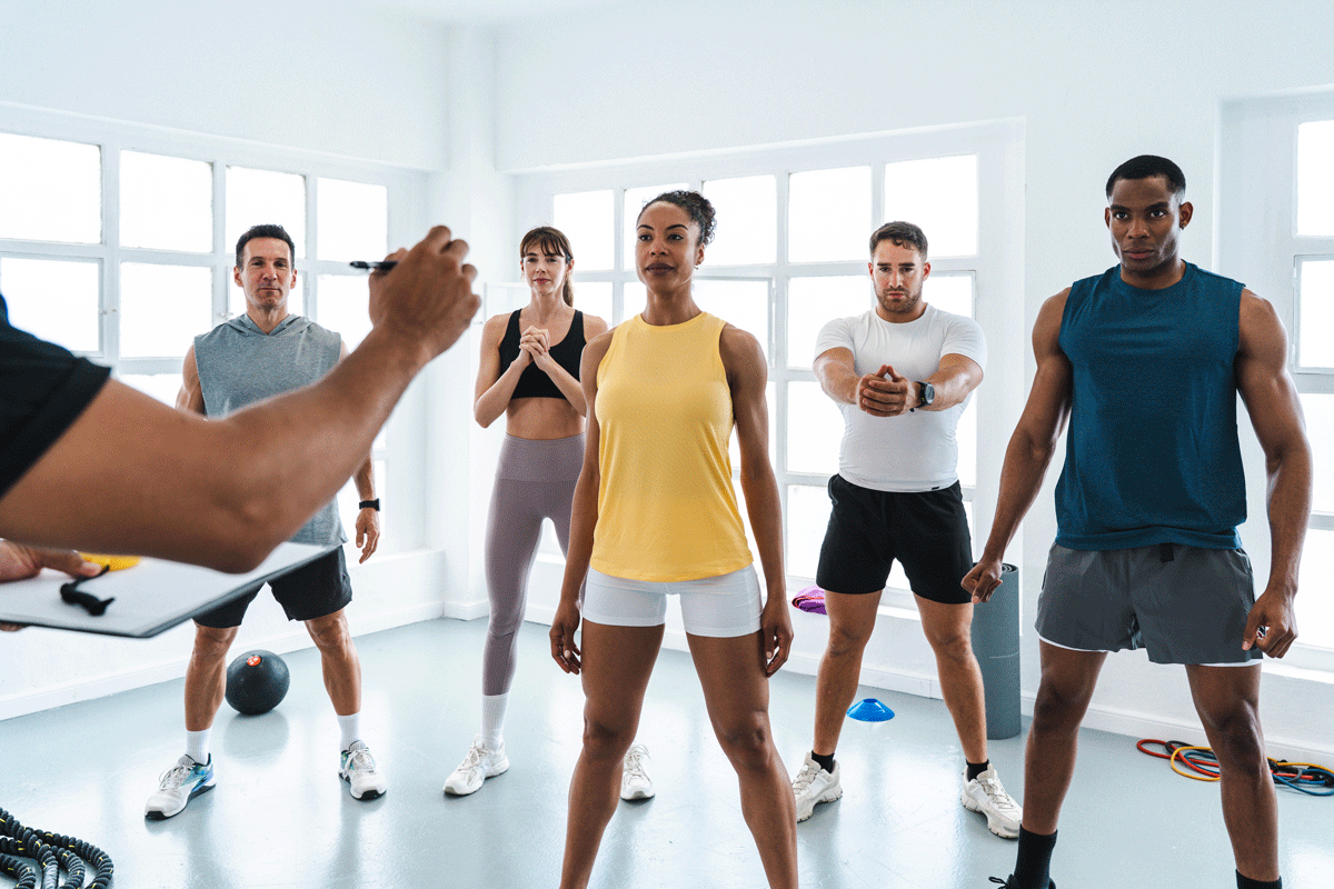 Fitness instructor giving instructions to a diverse group of five people during a workout class in a bright gym.