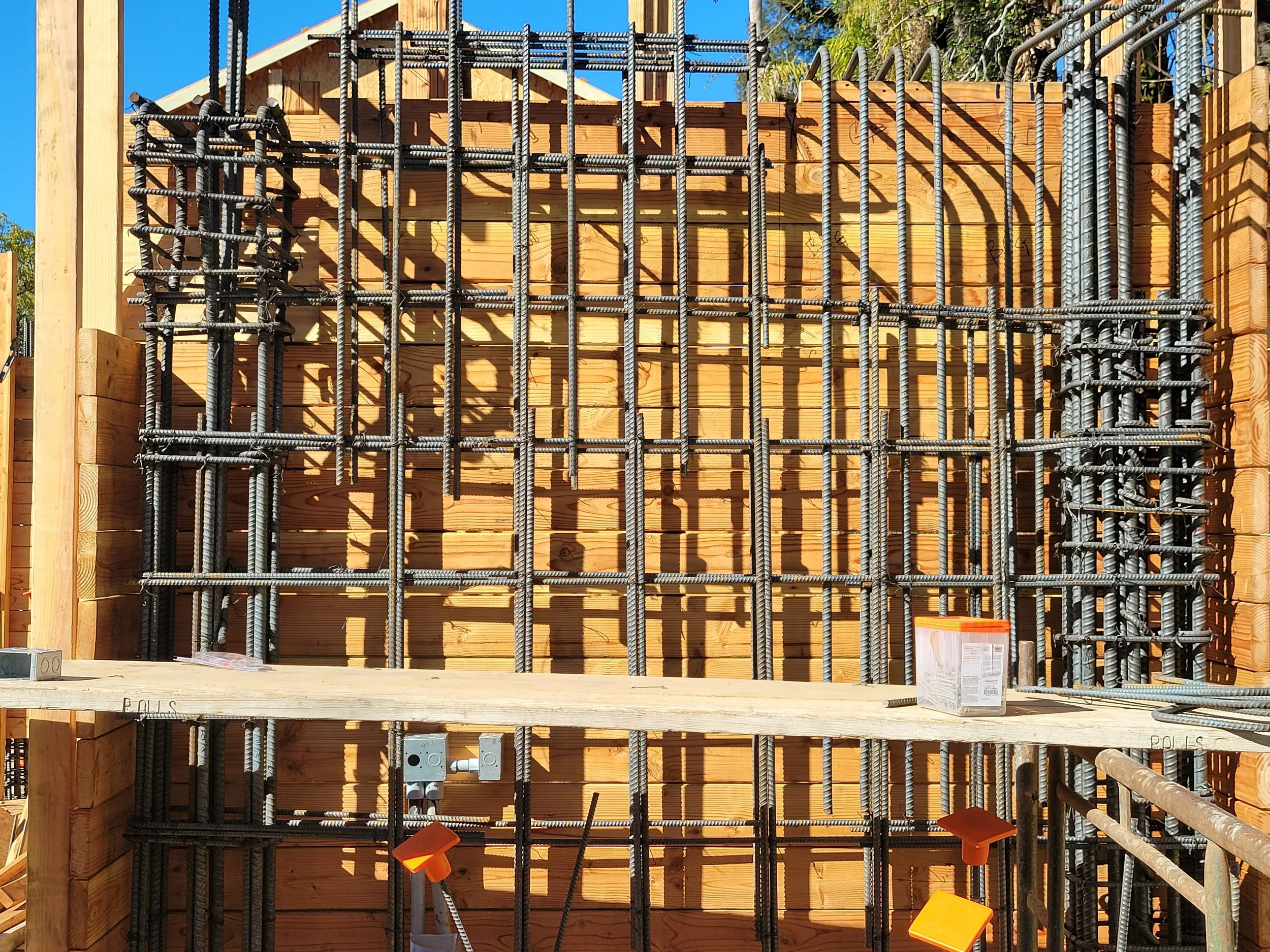 Construction site showing steel rebar framework and wooden formwork for a building foundation.