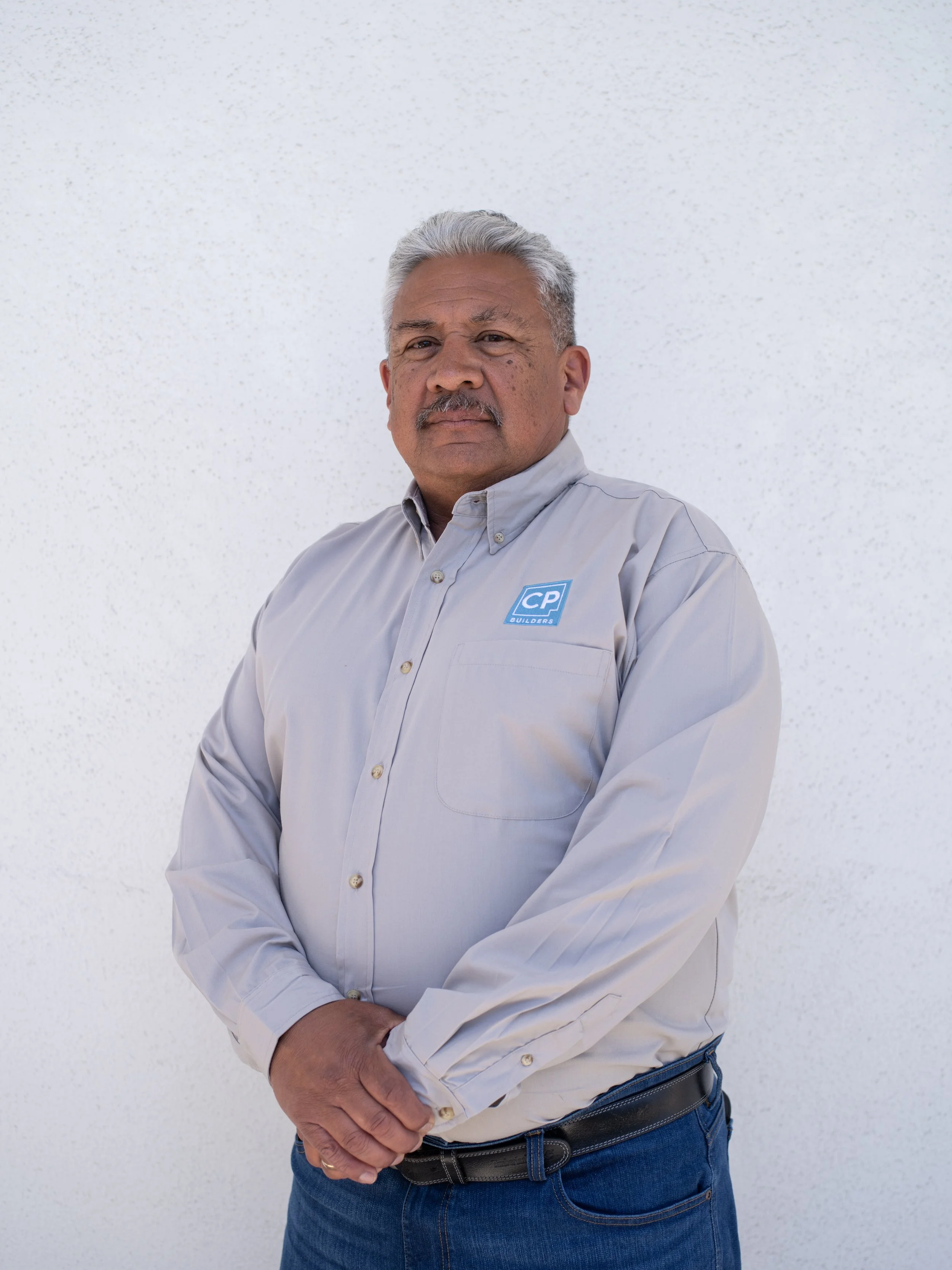 David is wearing a light gray button-up shirt with a CP Builders logo, standing against a plain white background.