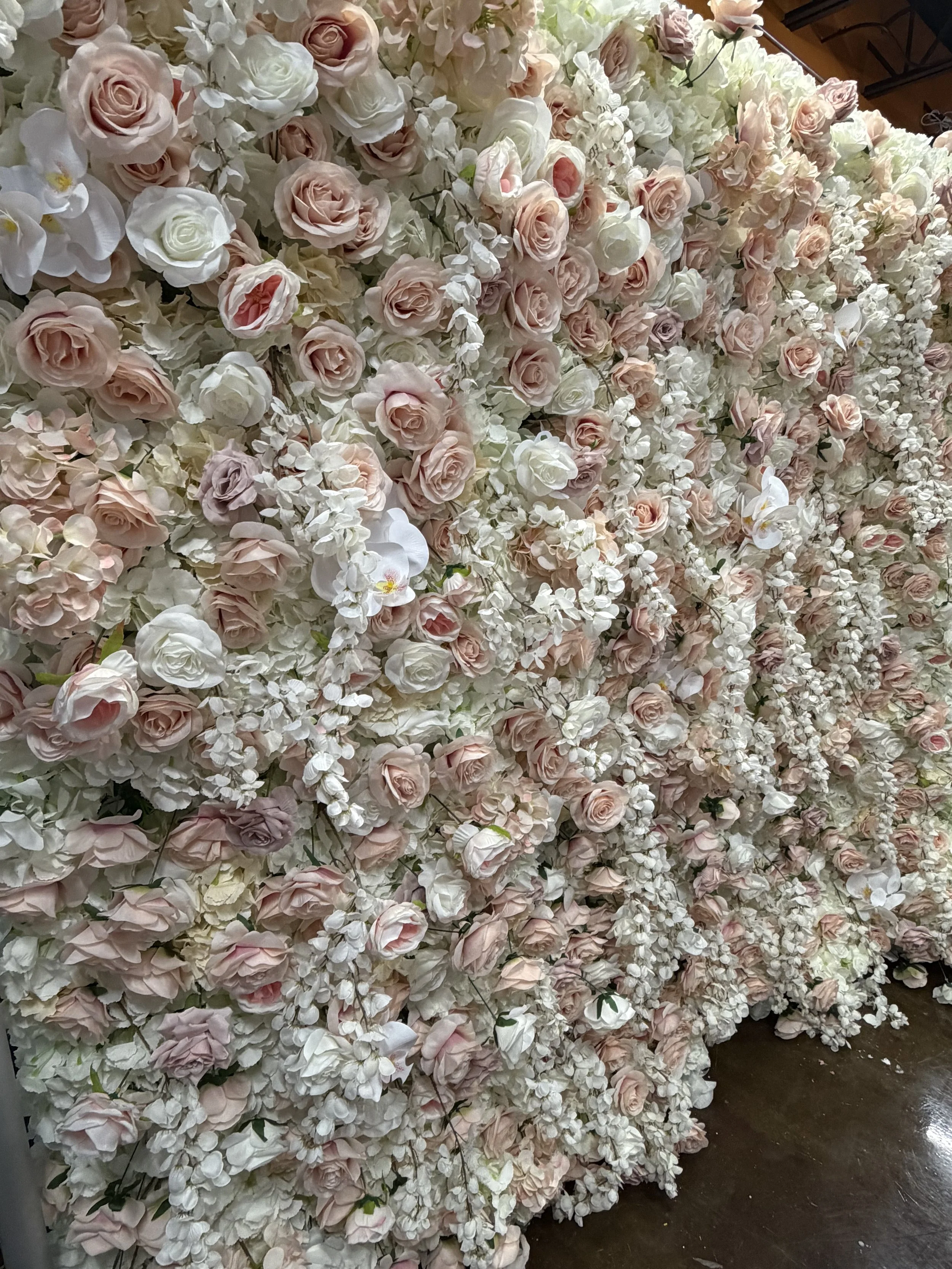 A large arrangement of pink and white roses, hydrangeas, and orchids in a floral wall display.