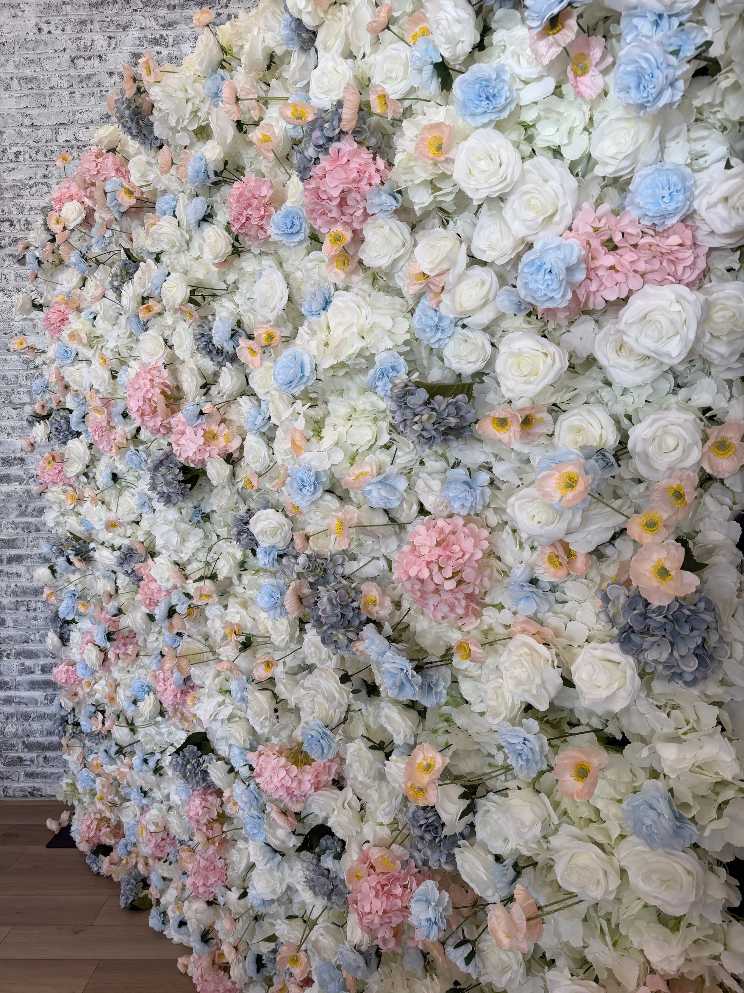 A floral wall decoration with white, pink, blue, and purple flowers against a gray brick wall background.
