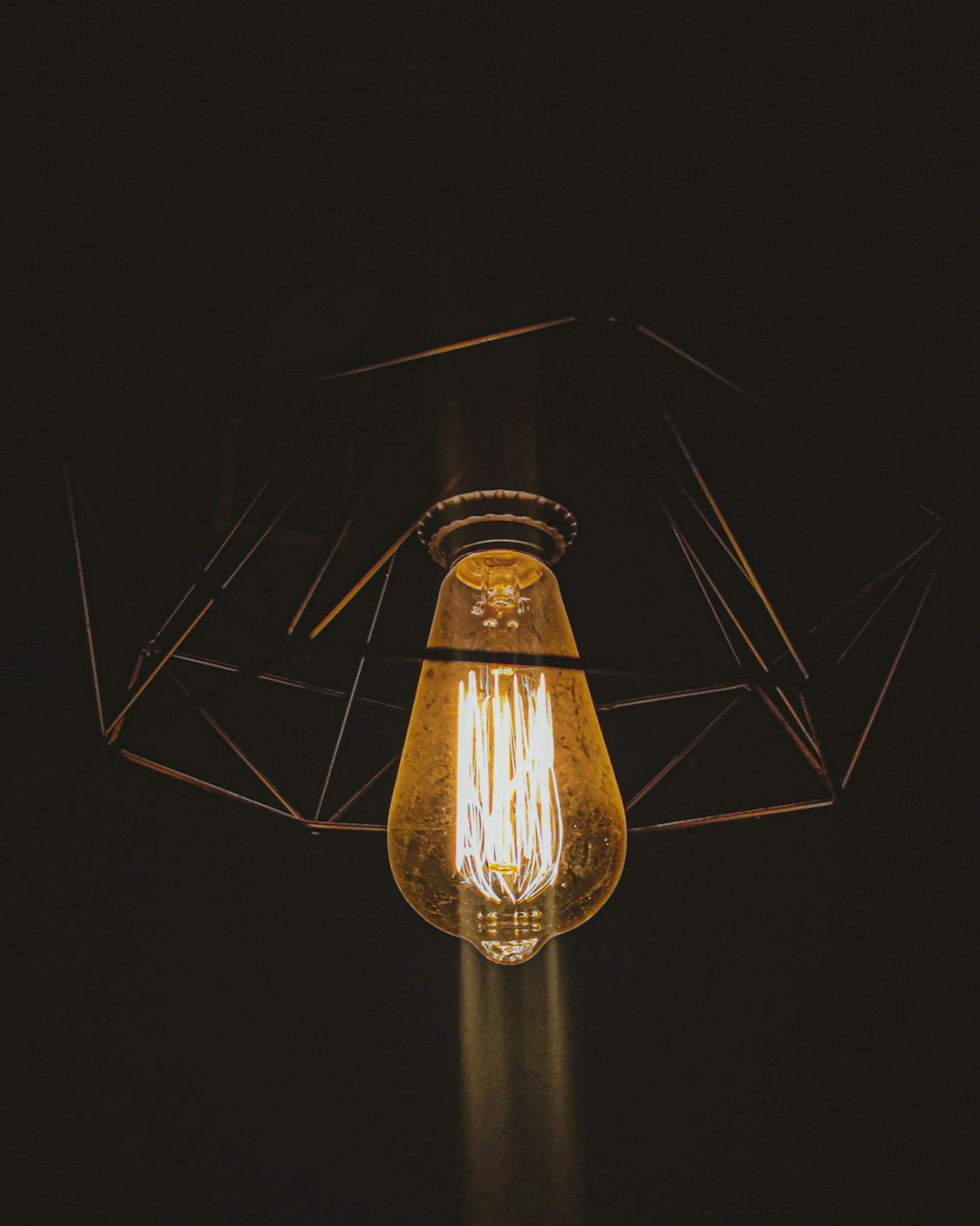 Close-up of an illuminated vintage filament light bulb against a dark background.