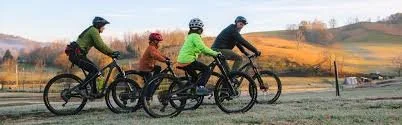 Four people riding bikes along a scenic trail with open fields and hills in the background.