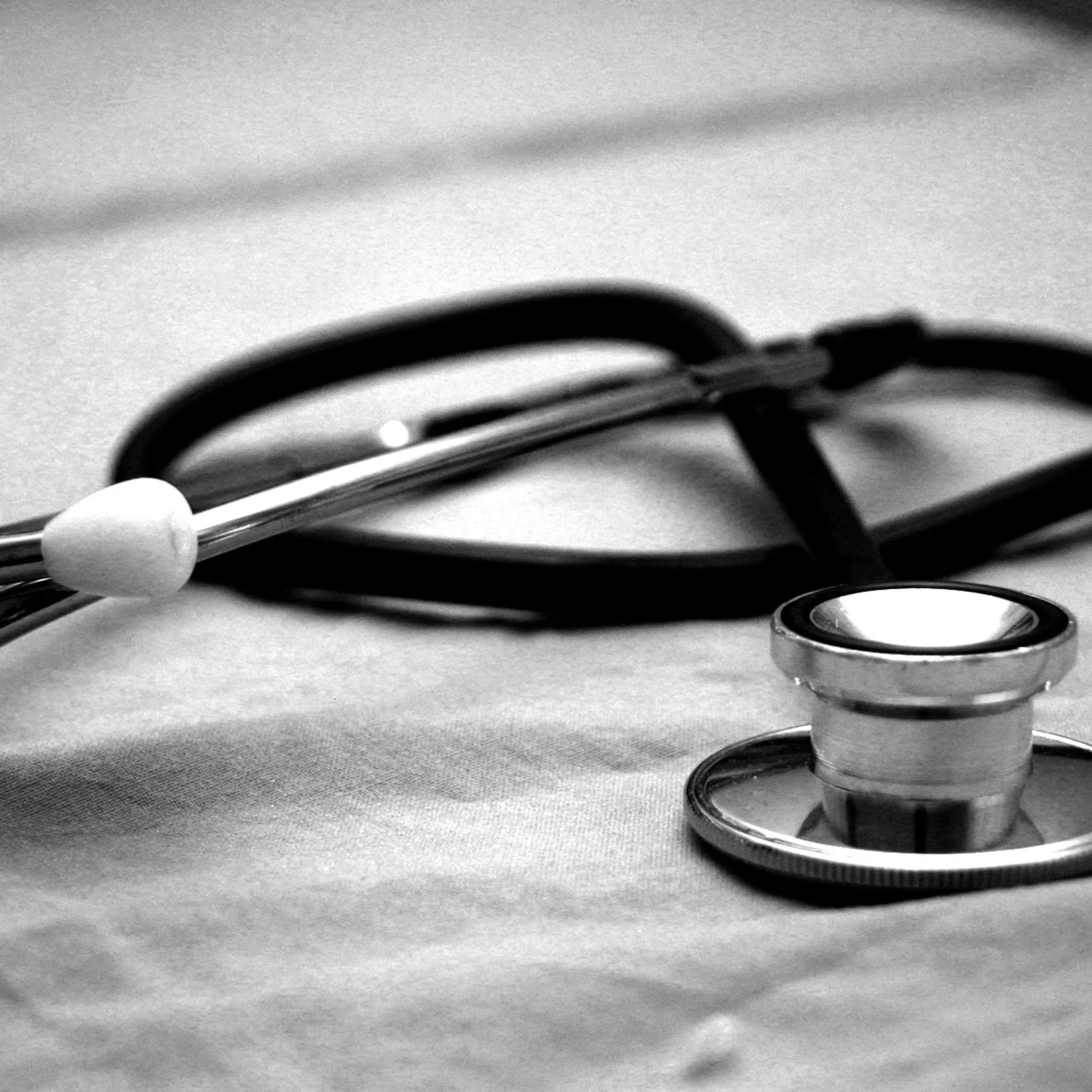 A stethoscope lying on a surface with a pen resting on top of it, all in black and white.